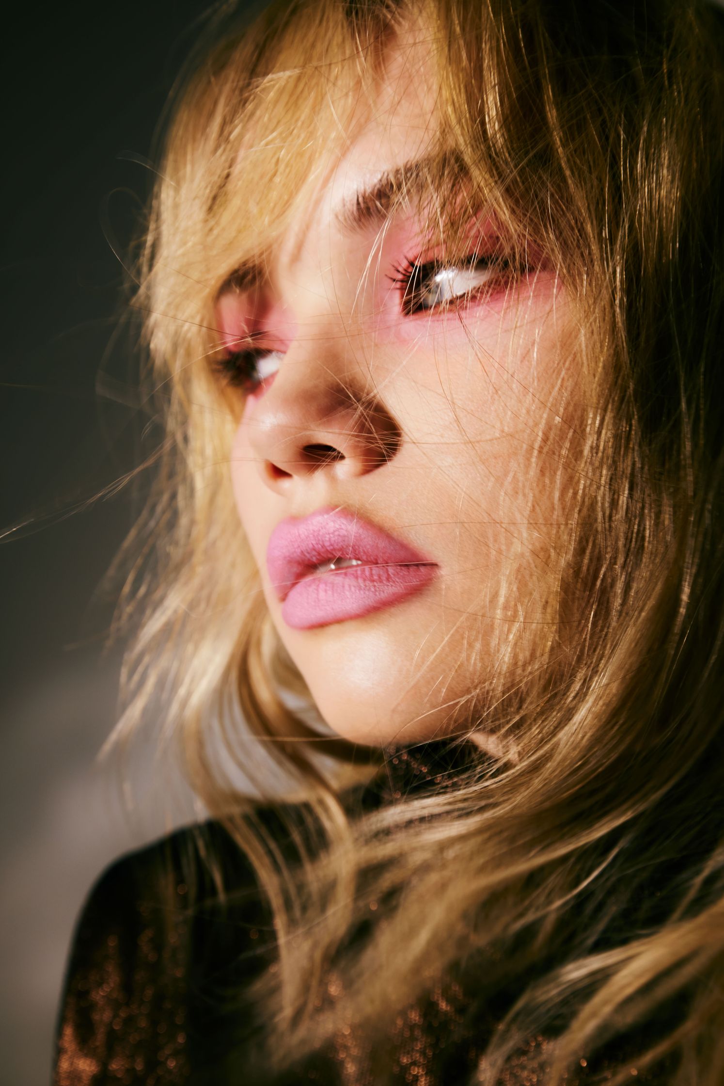 a woman with pink eye makeup is posing in front of a dark background