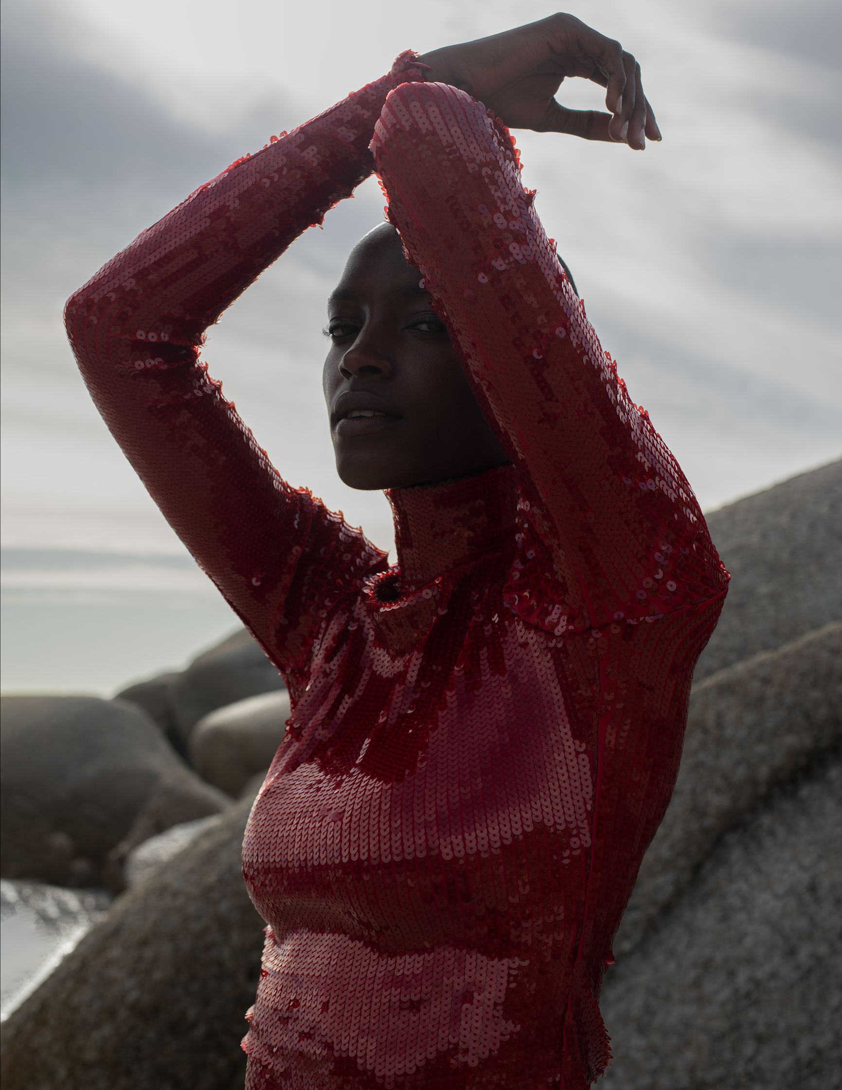 a black woman in a red sequined top posing on rocks