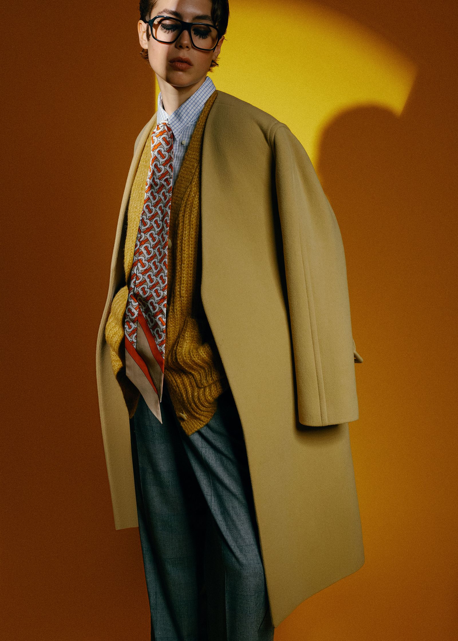 a young man in a beige coat posing for a photo
