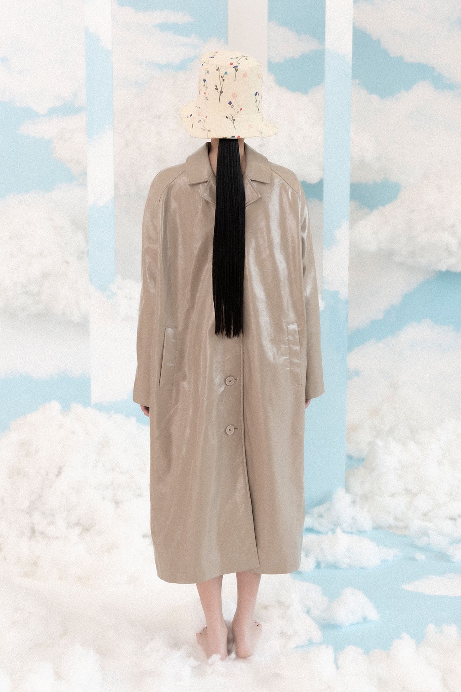 a woman in a trench coat standing in front of clouds