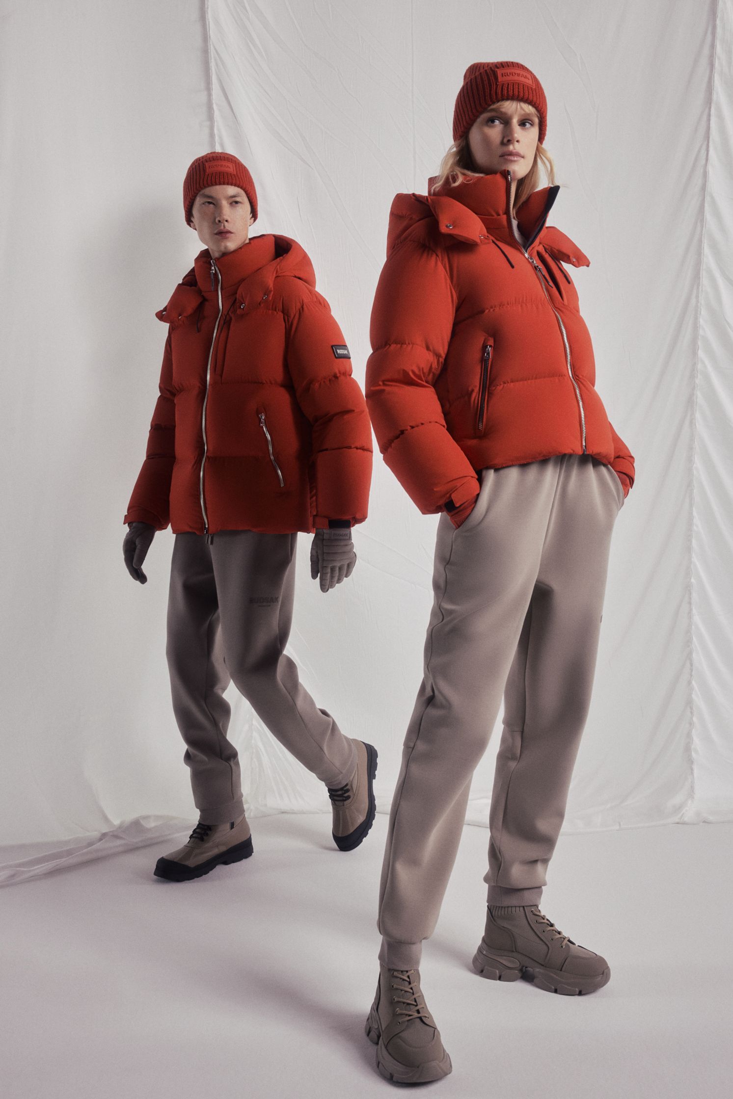 two women in red puffer jackets and hats standing in front of a white background