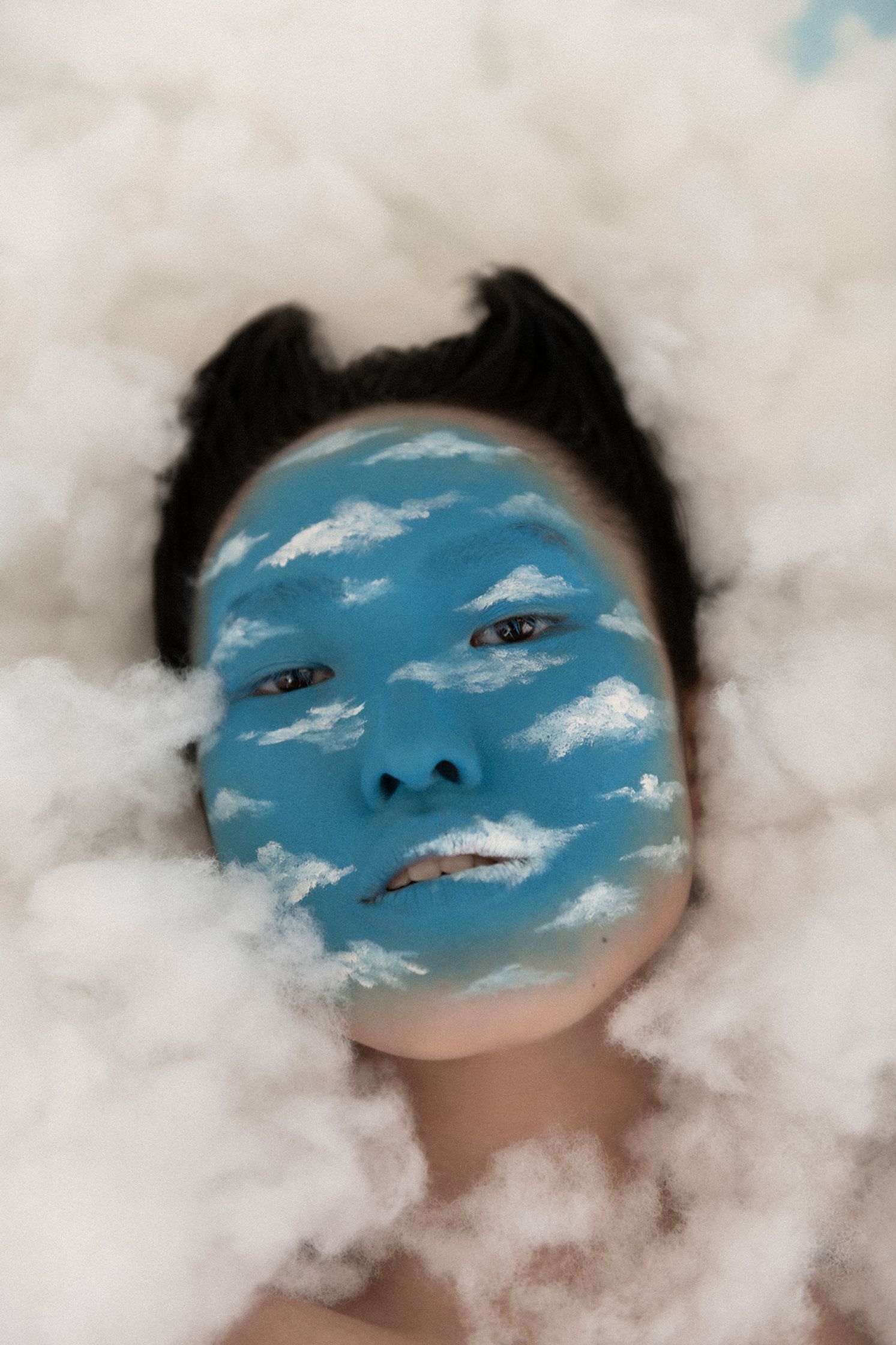 a woman laying on a cloud with blue paint on her face