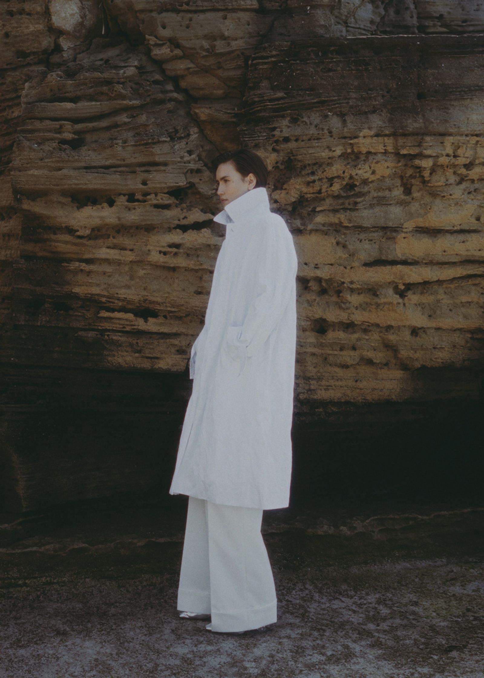 a man in a white coat standing in front of rocks
