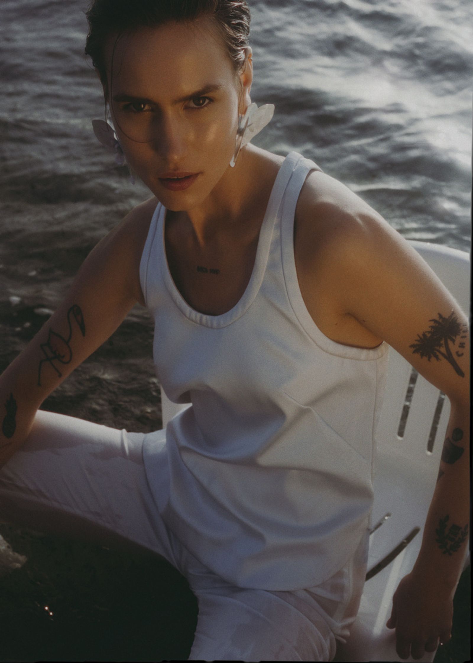 a woman in a white tank top sitting on a chair by the water