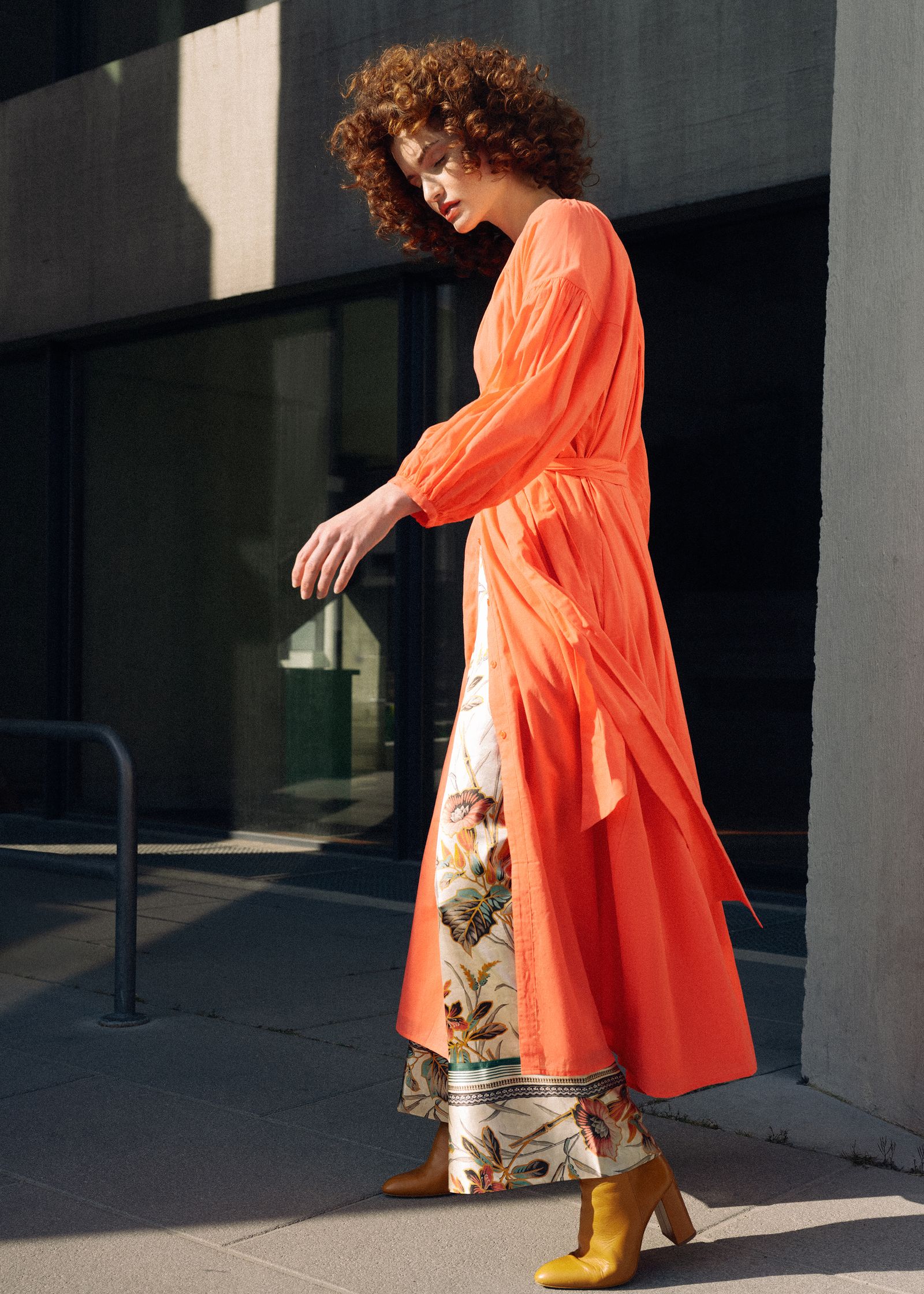 a woman in an orange coat walking down the street