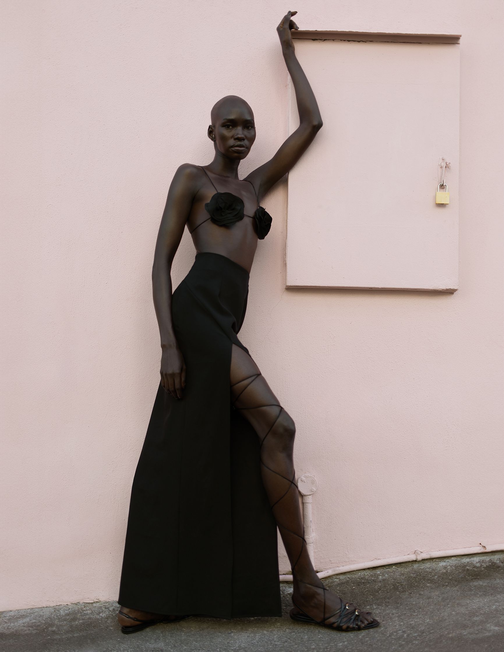 a woman in a black dress leaning against a pink wall