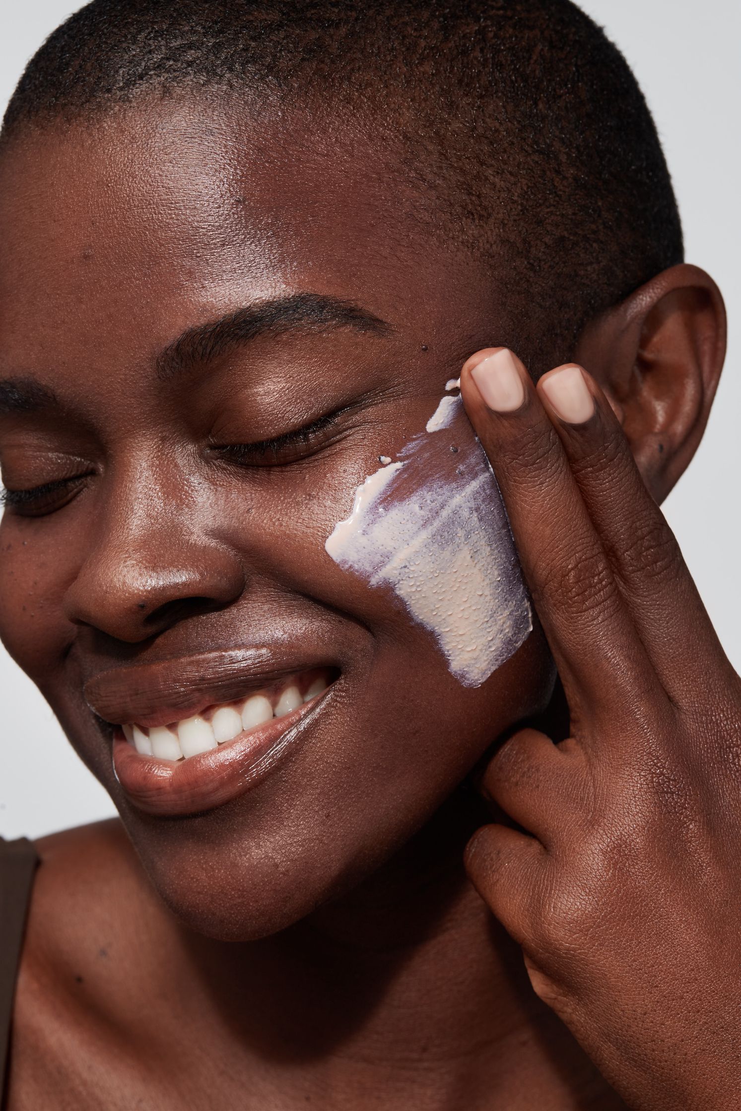 a woman is smiling while applying a cream to her face