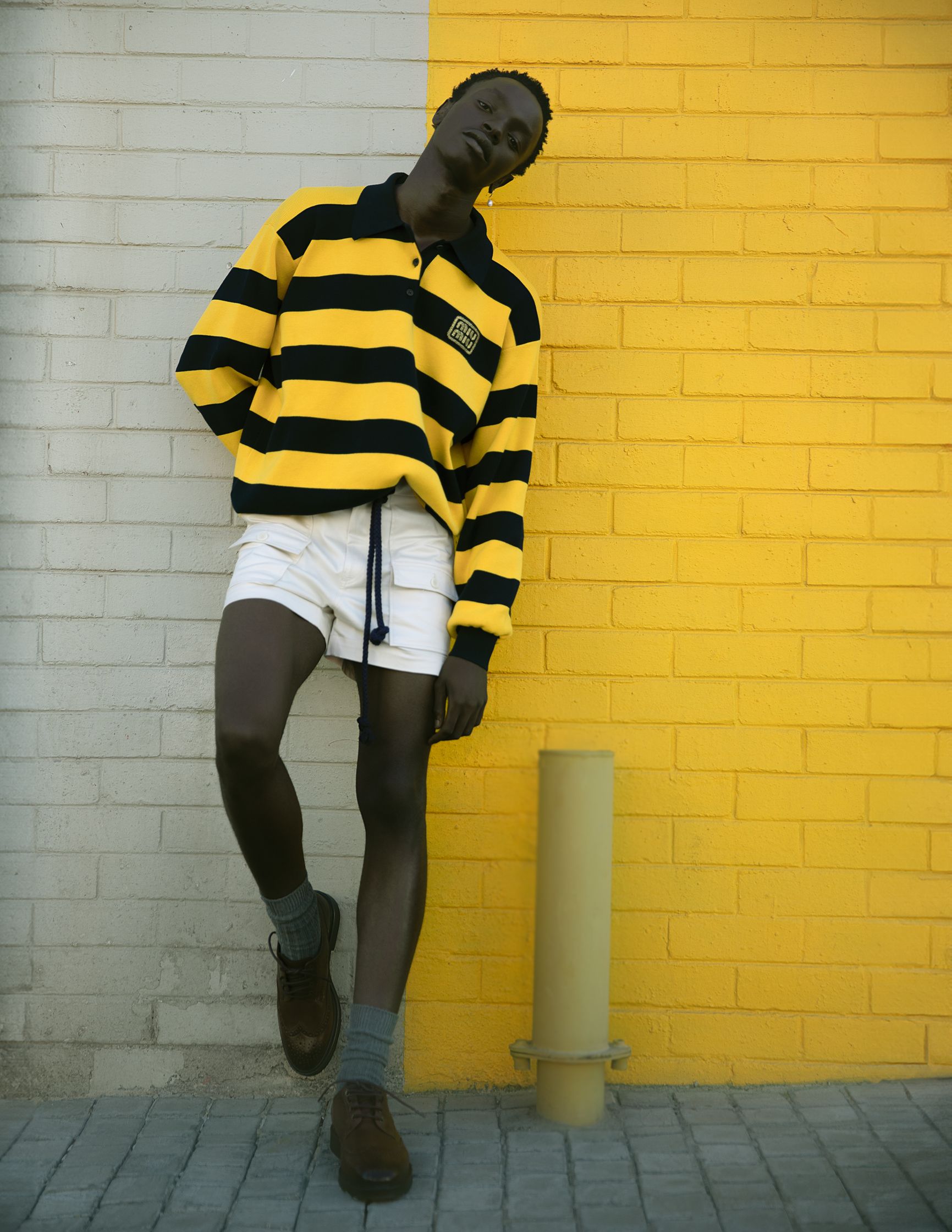 a man in a yellow striped shirt leaning against a yellow wall