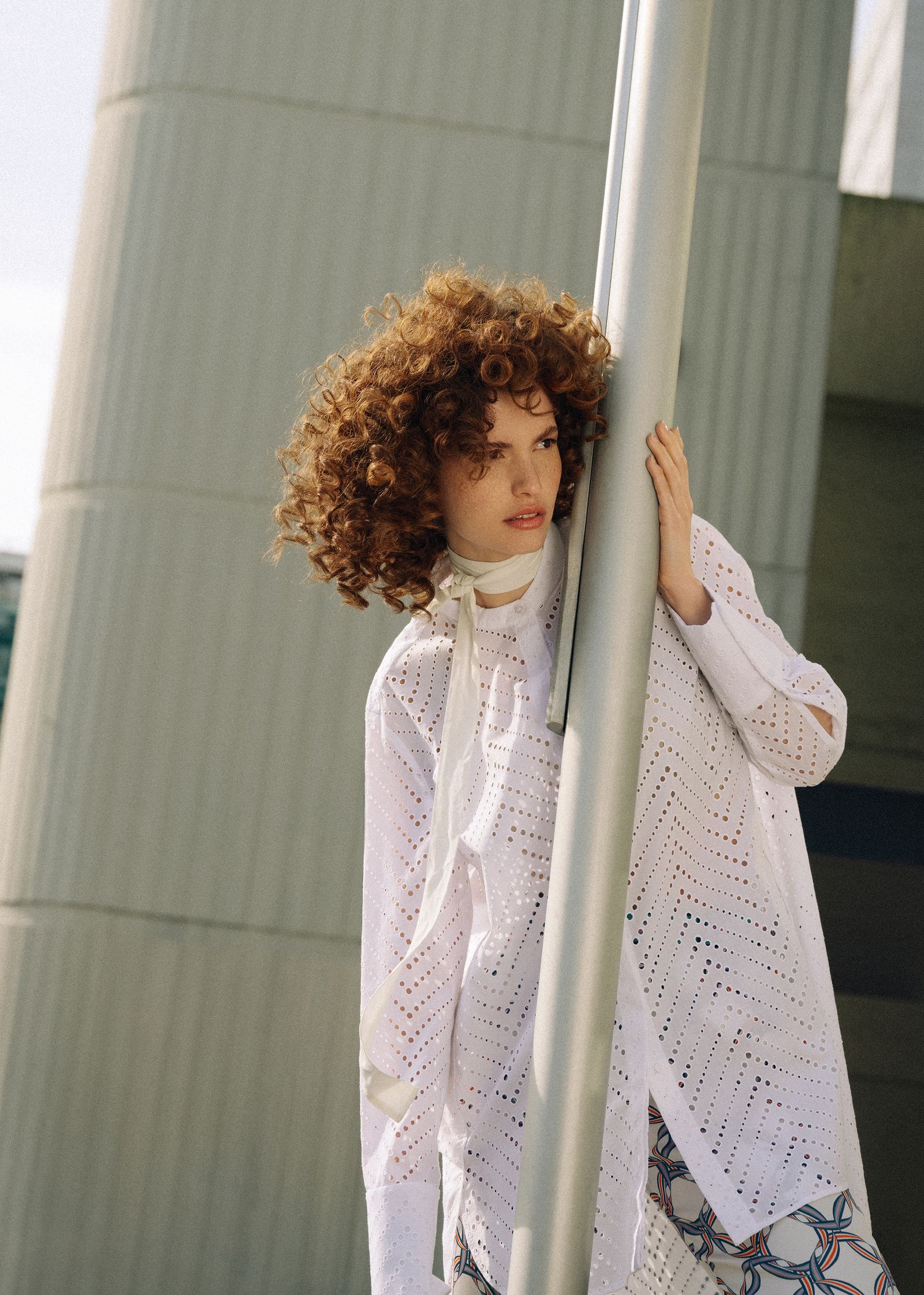 a woman with curly hair leaning against a pole