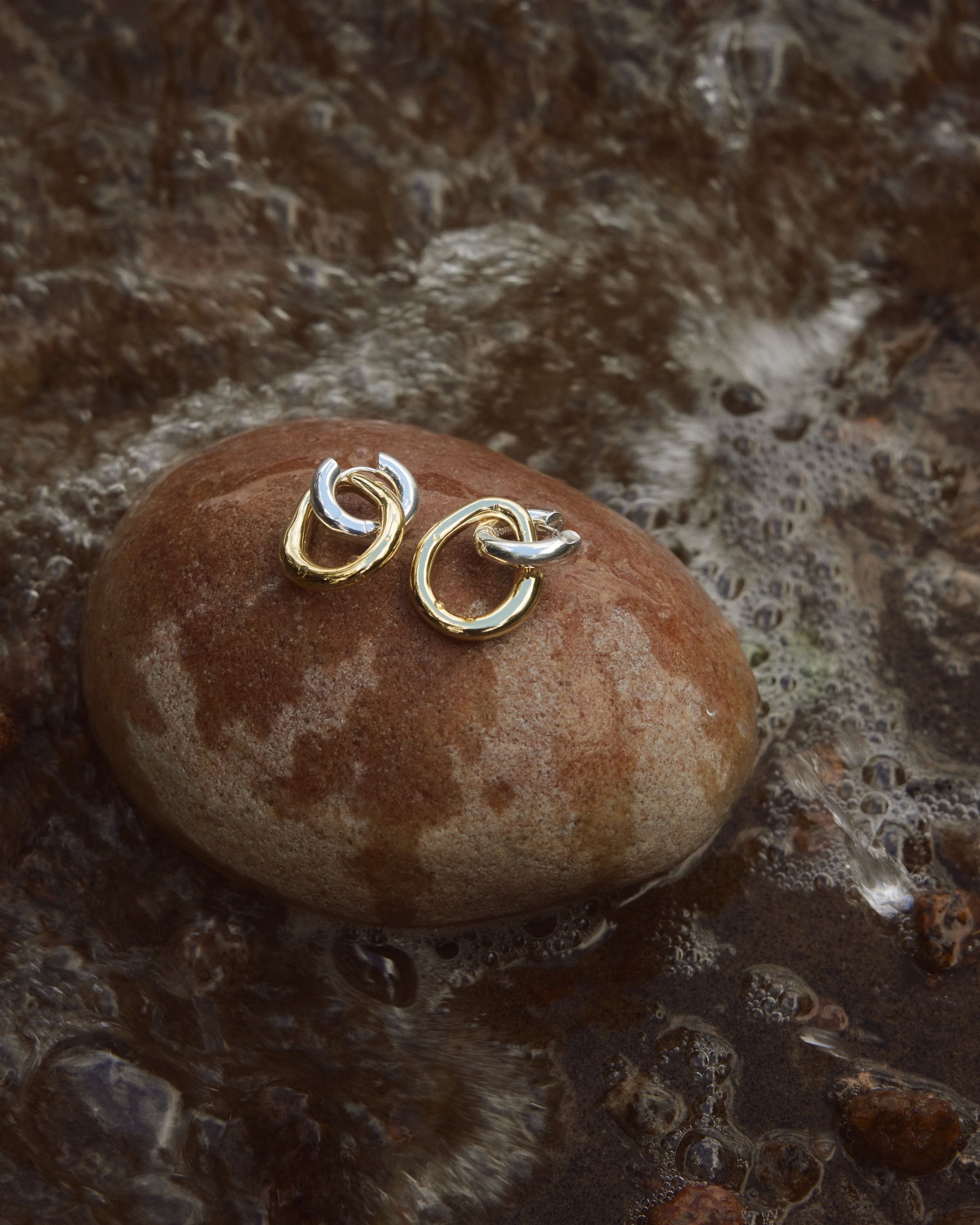 a pair of earrings sitting on a rock in the water