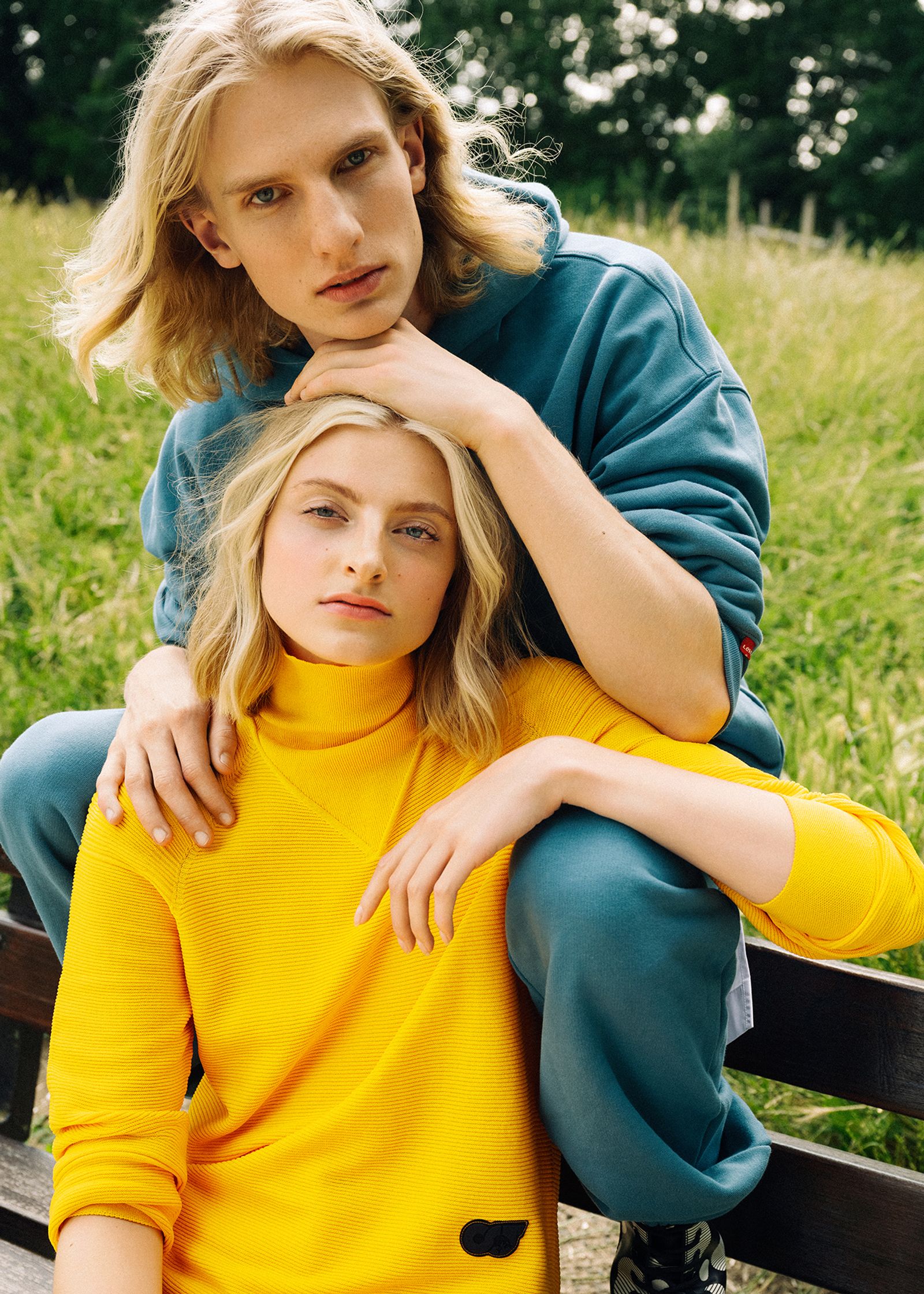a man and a woman sitting on a bench in a field