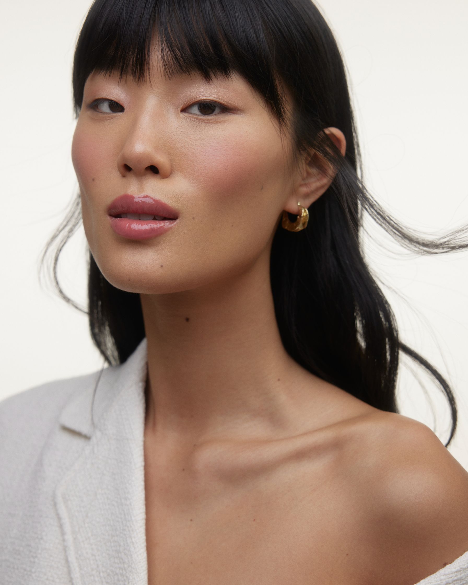 an asian woman wearing a white jacket and earrings