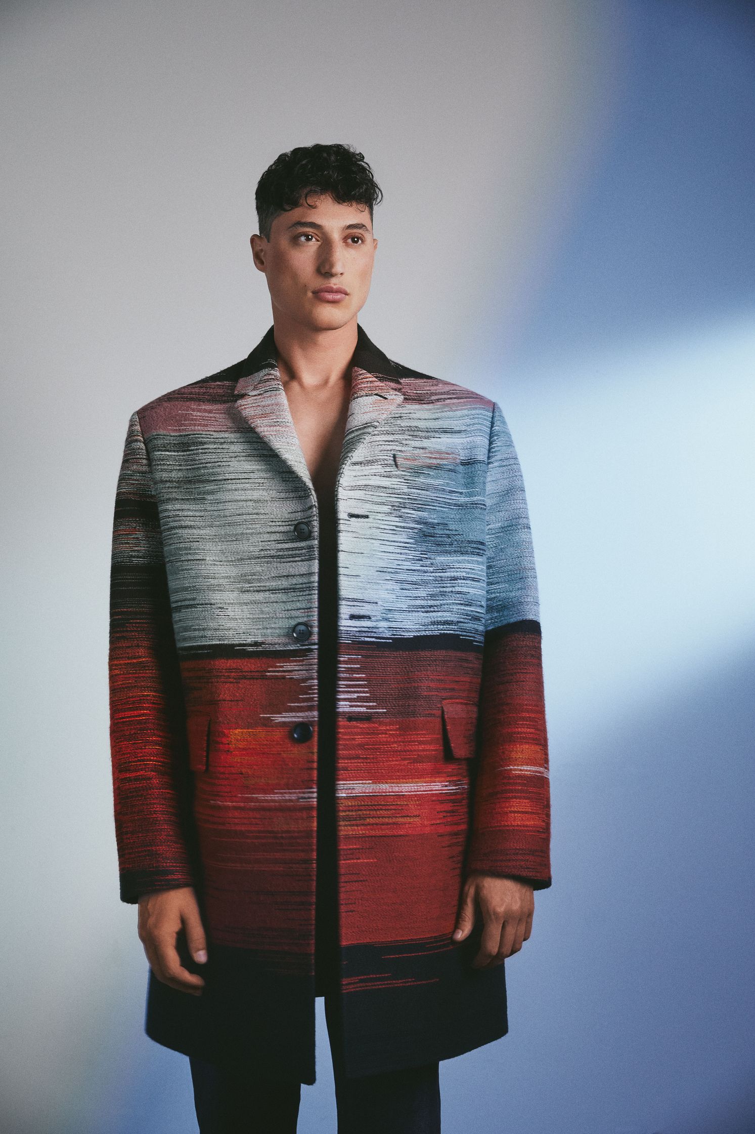 a man in a colorful coat standing in front of a blue background
