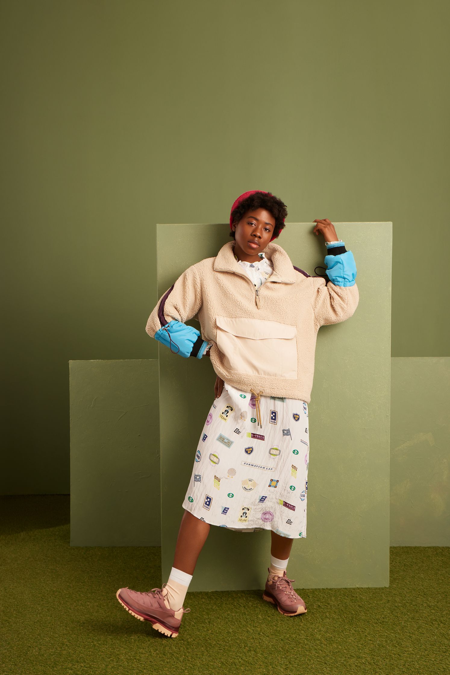 a woman wearing a sweater and skirt posing in front of a green wall