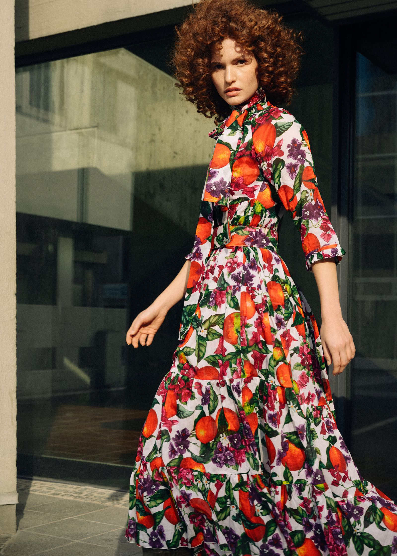 a woman in an orange print dress walking down the street