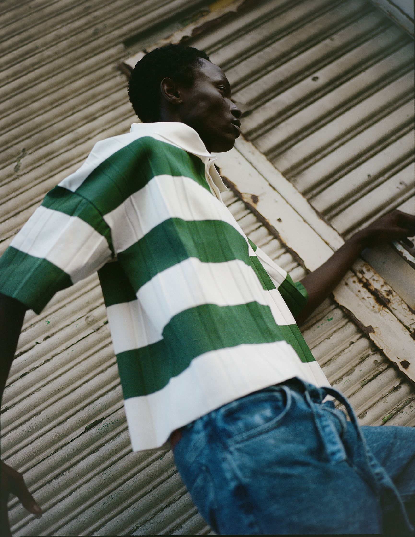 a man in a green and white striped shirt leaning against a wall