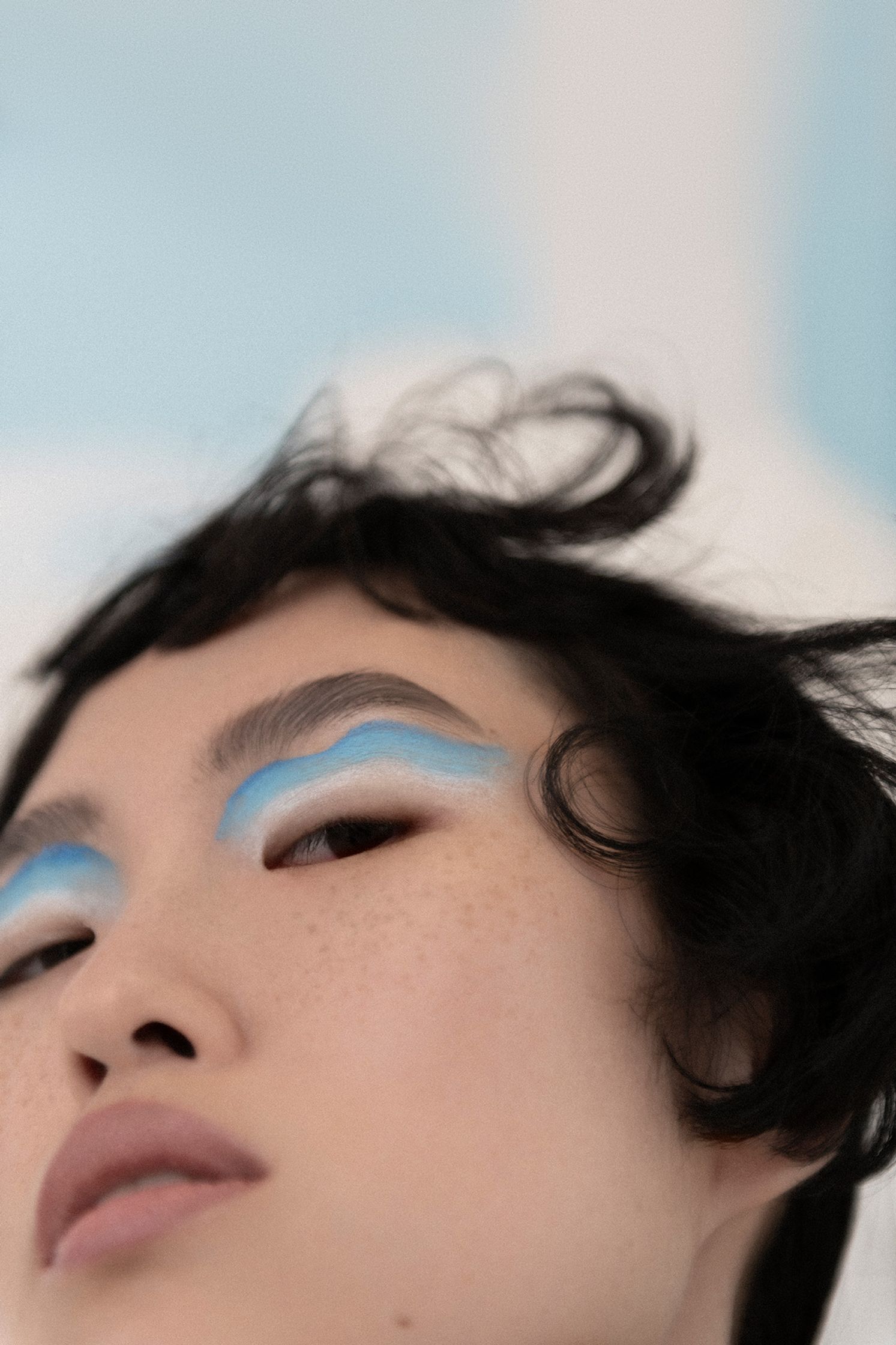 a woman with blue eye makeup laying on a bed