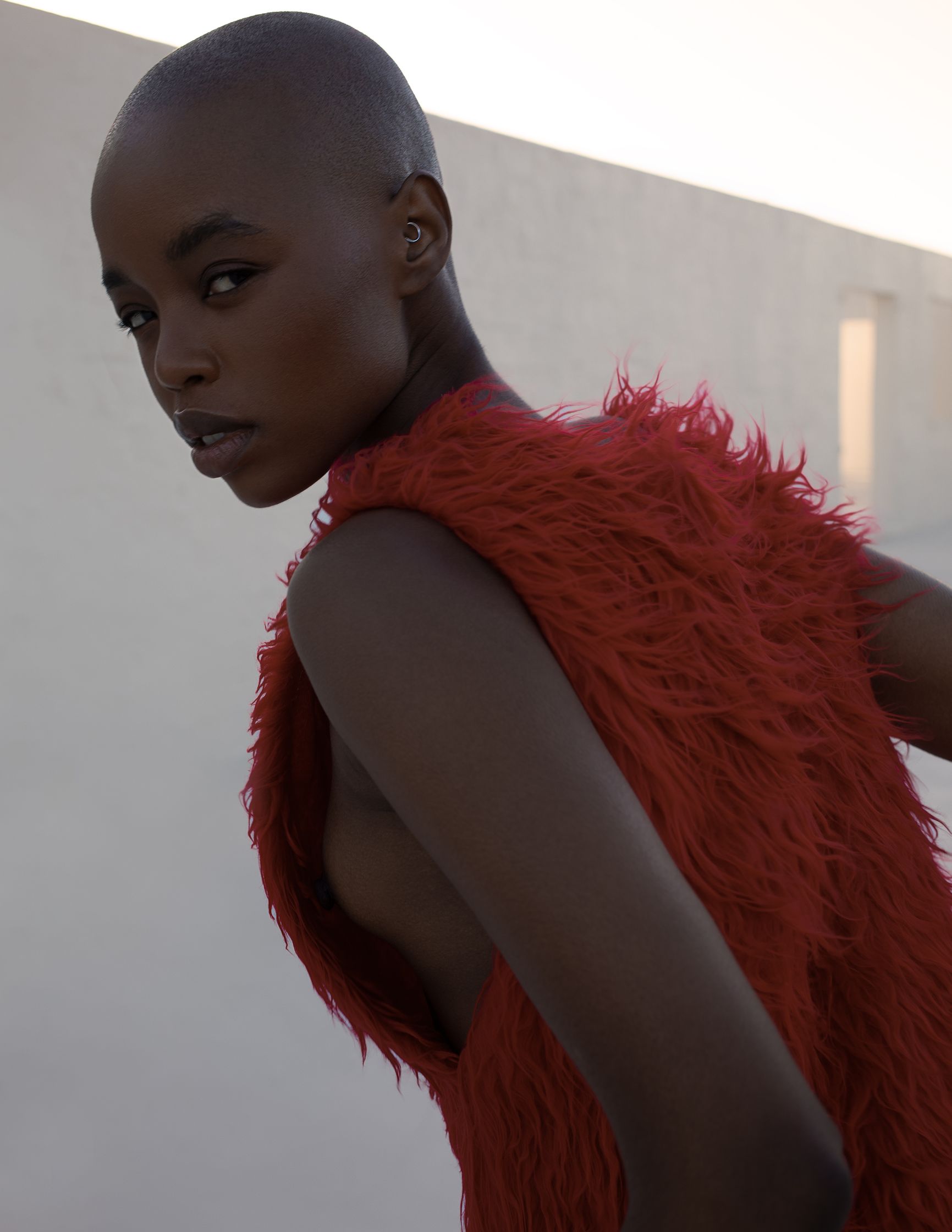 a black woman in a red fur coat posing in front of a white wall