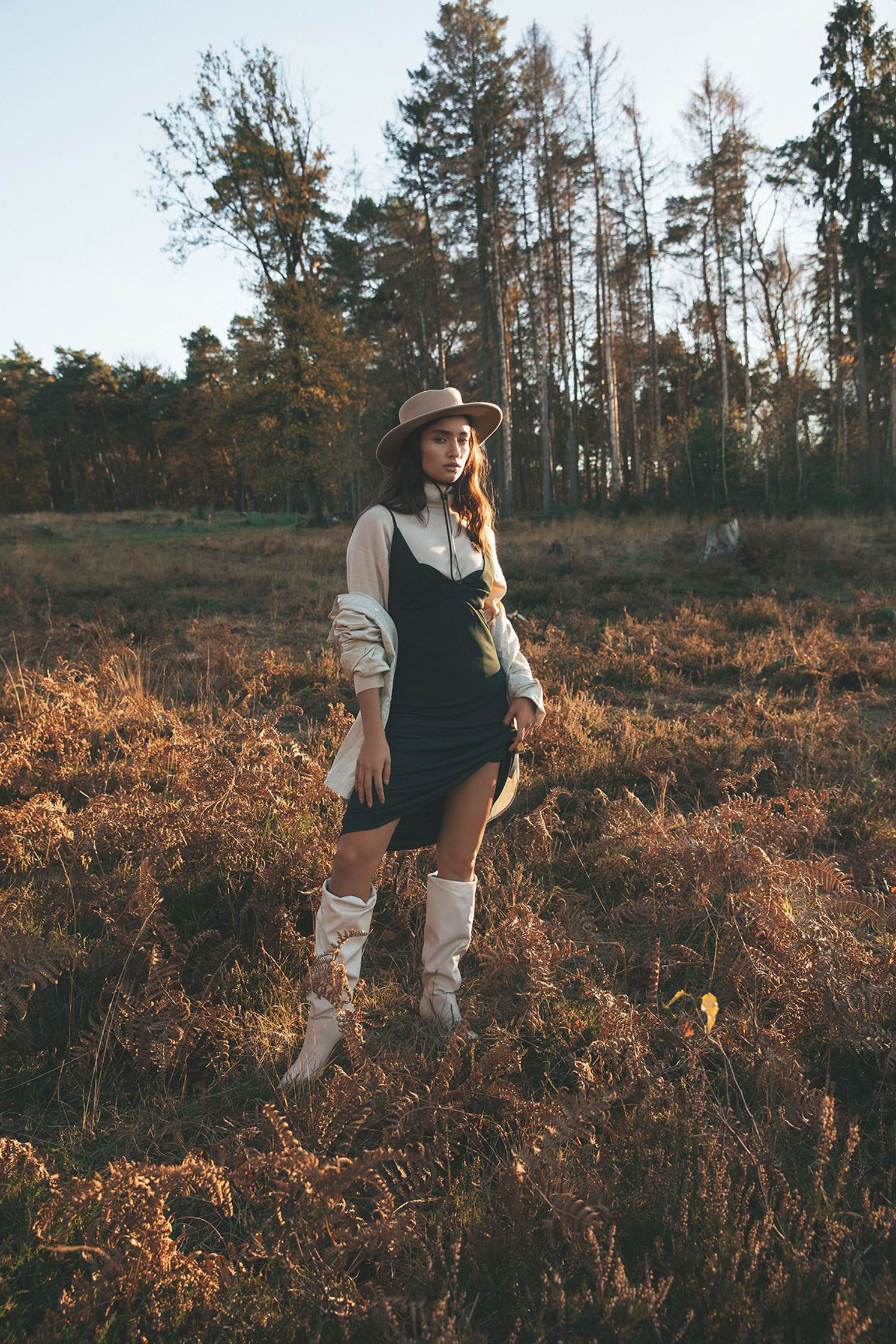 a woman in a hat and boots standing in a field