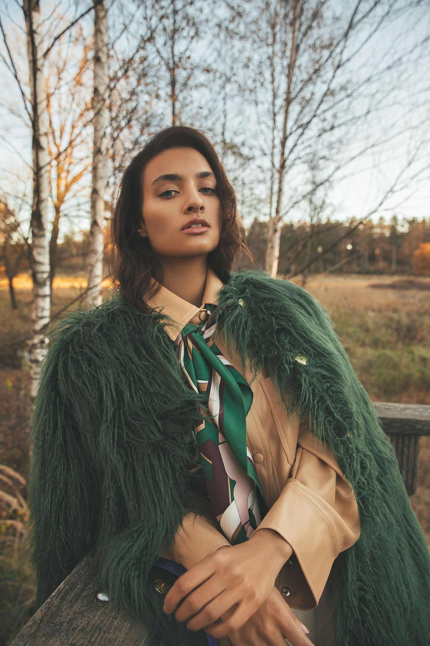 a woman in a green fur coat posing on a wooden bench