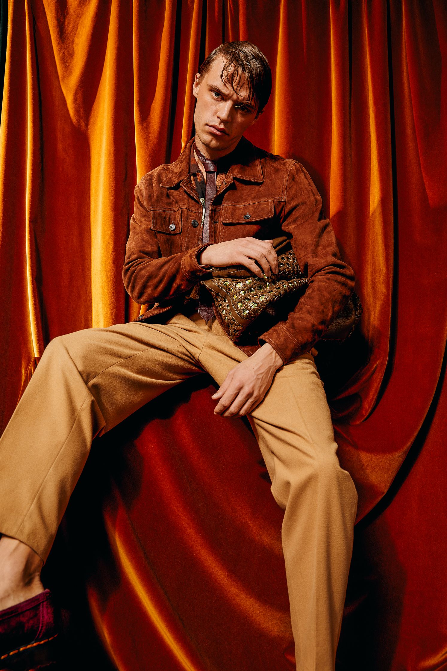 a man in a tan jacket sitting on top of a red curtain