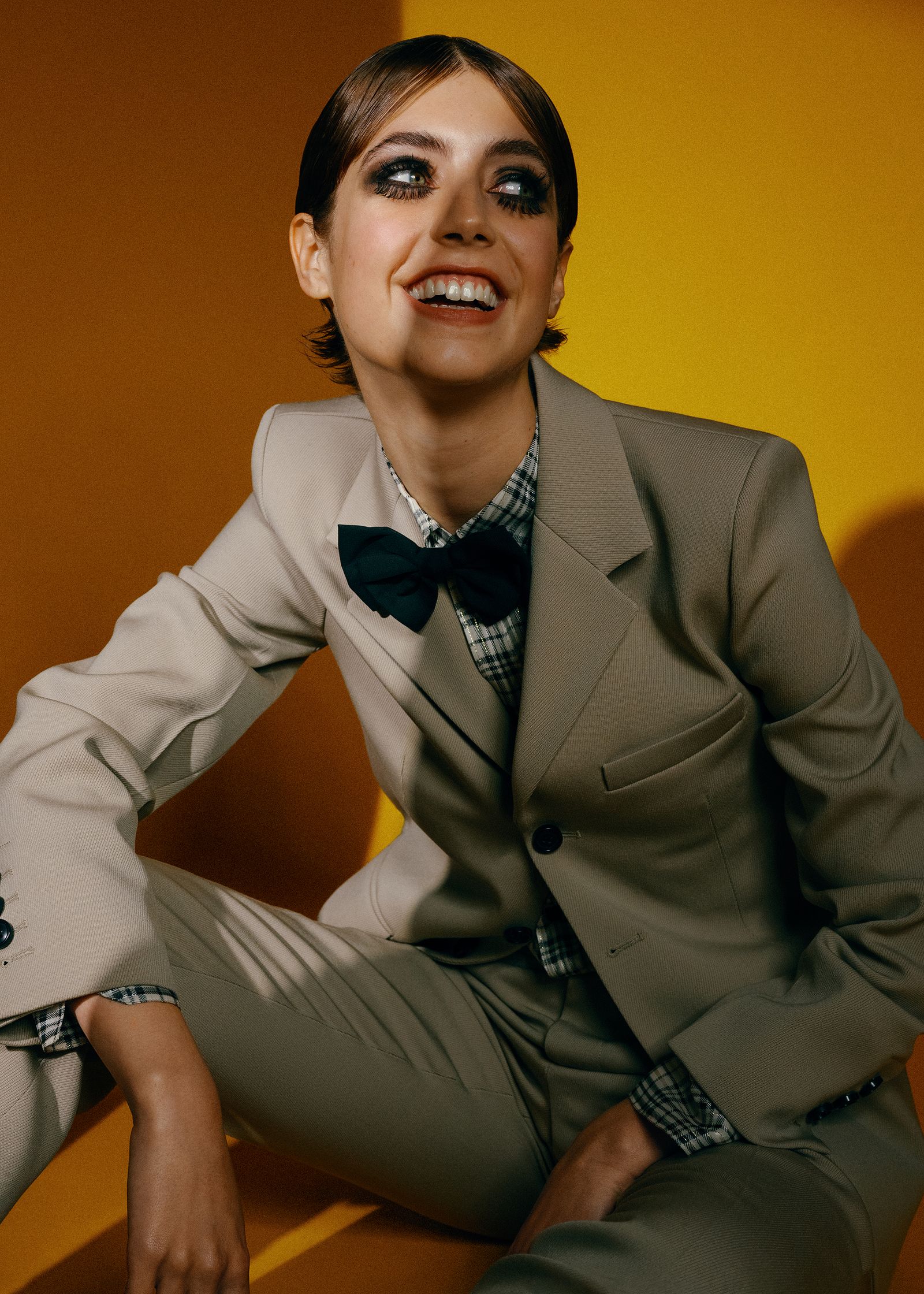 a woman in a tan suit sitting on a yellow background