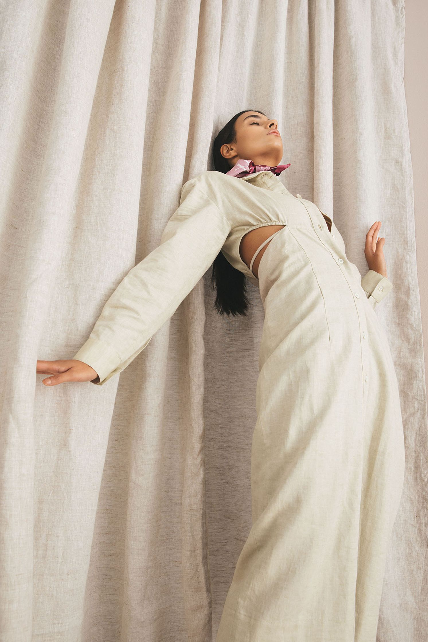 a woman in a white jumpsuit leaning against a curtain