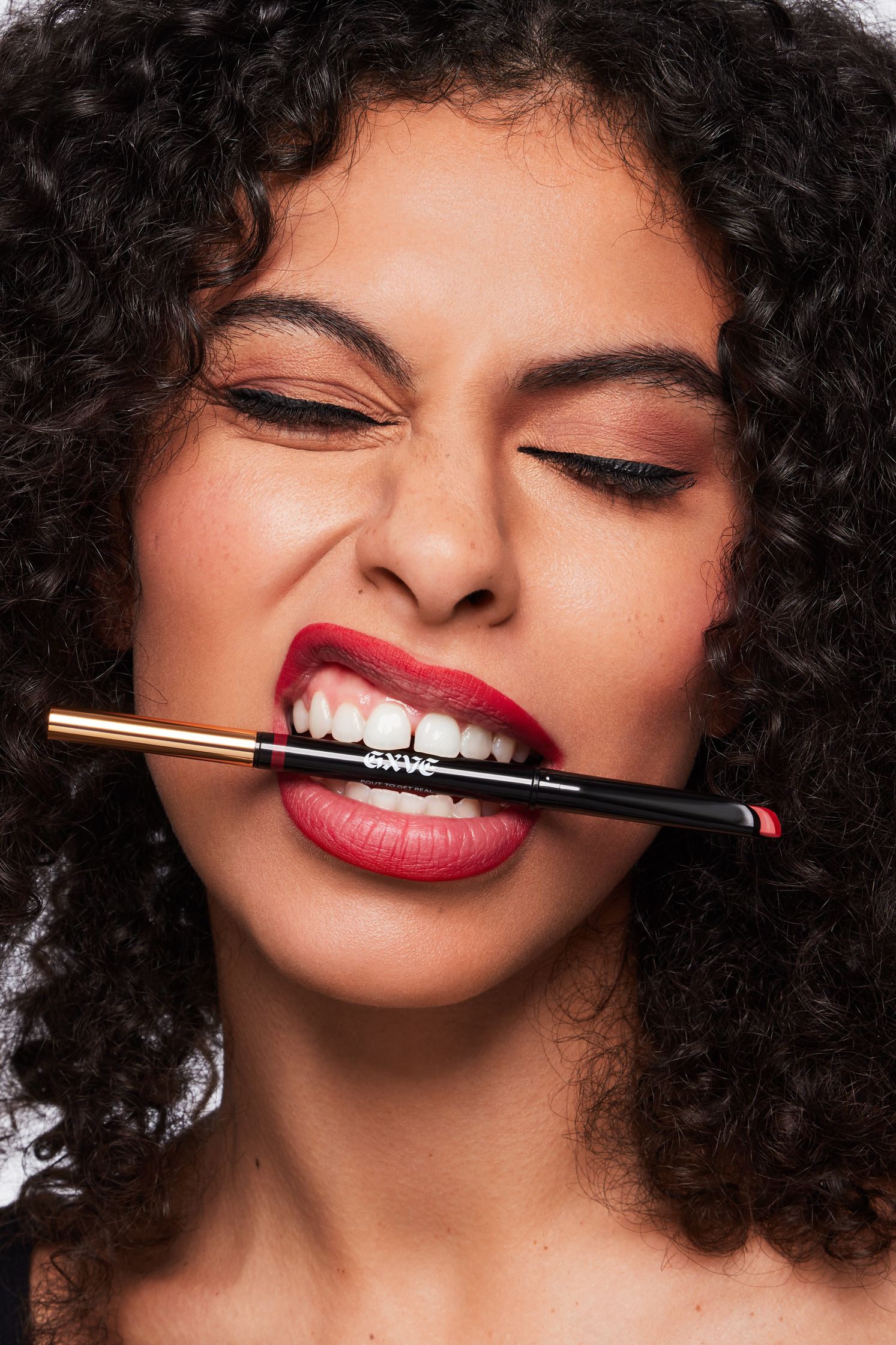a woman with curly hair is holding a lipstick in her mouth