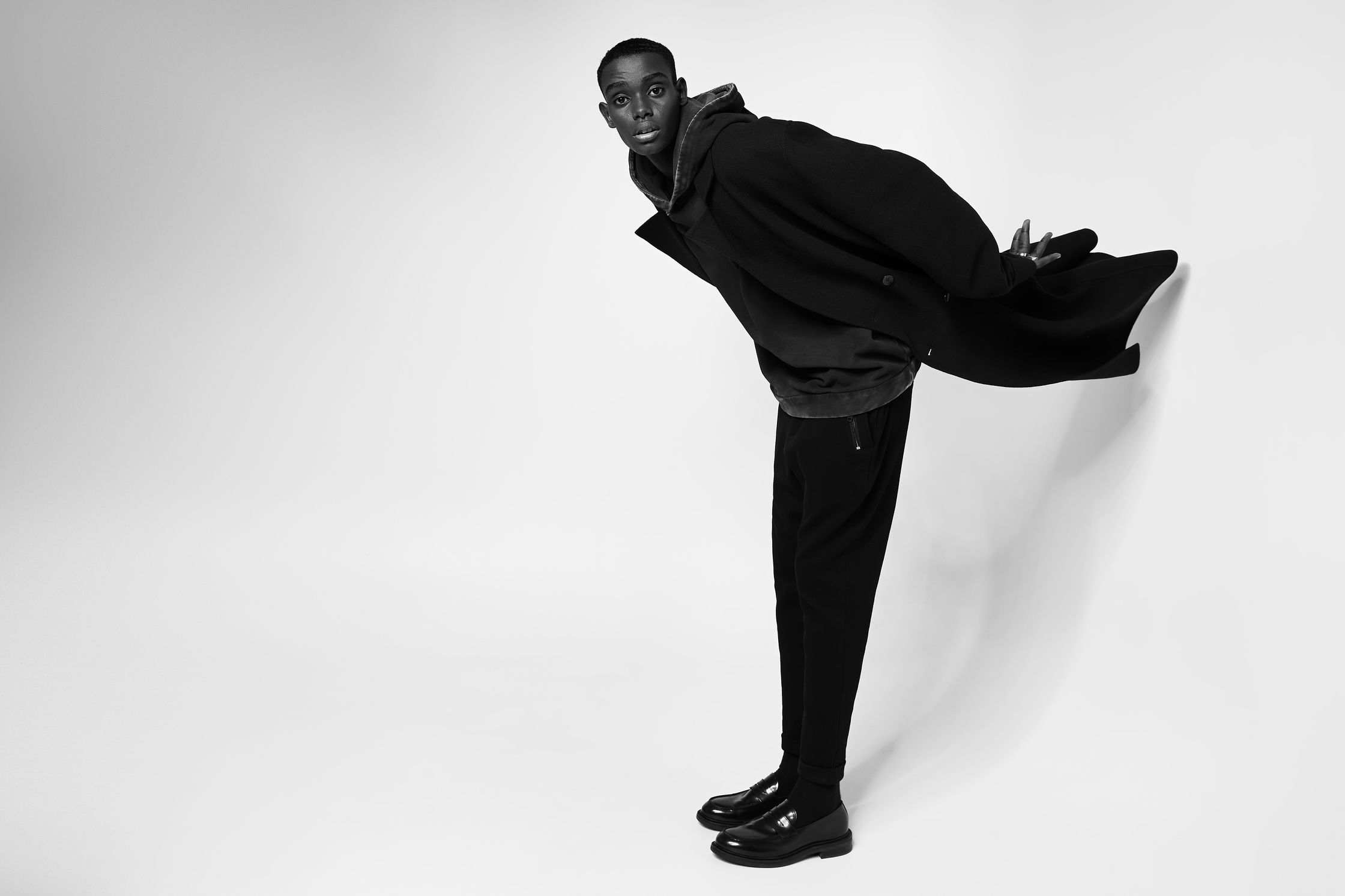 a man in a black coat leaning against a wall