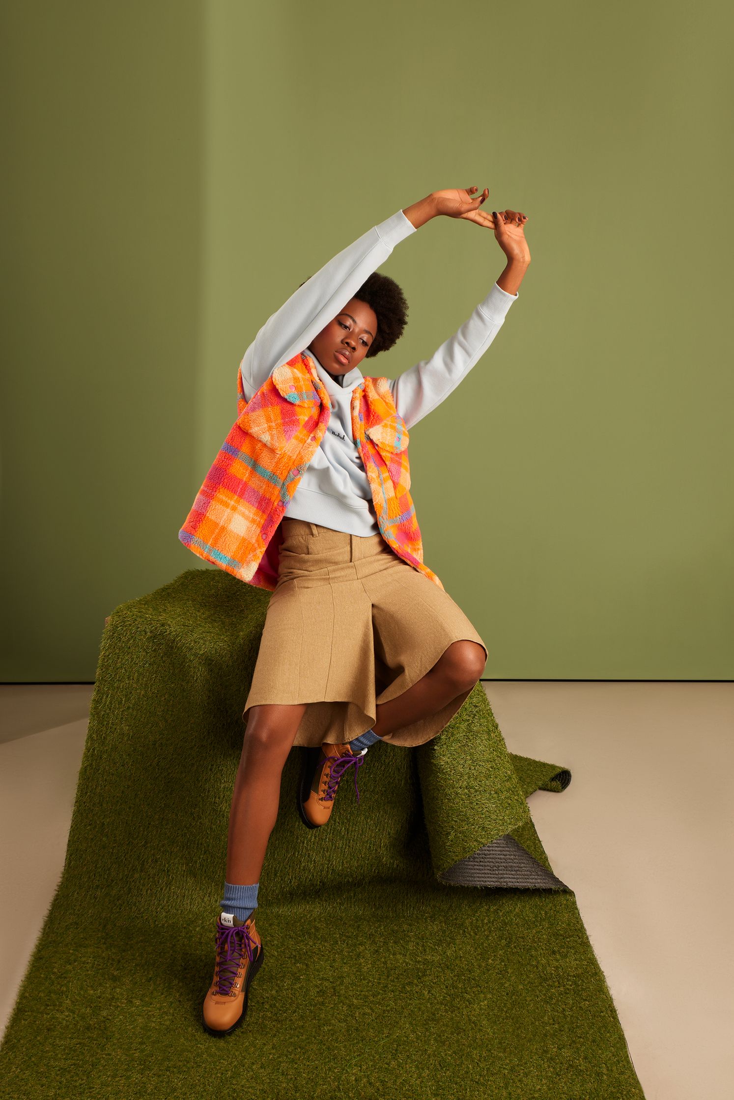 a woman in a plaid shirt and shorts is posing on a green carpet