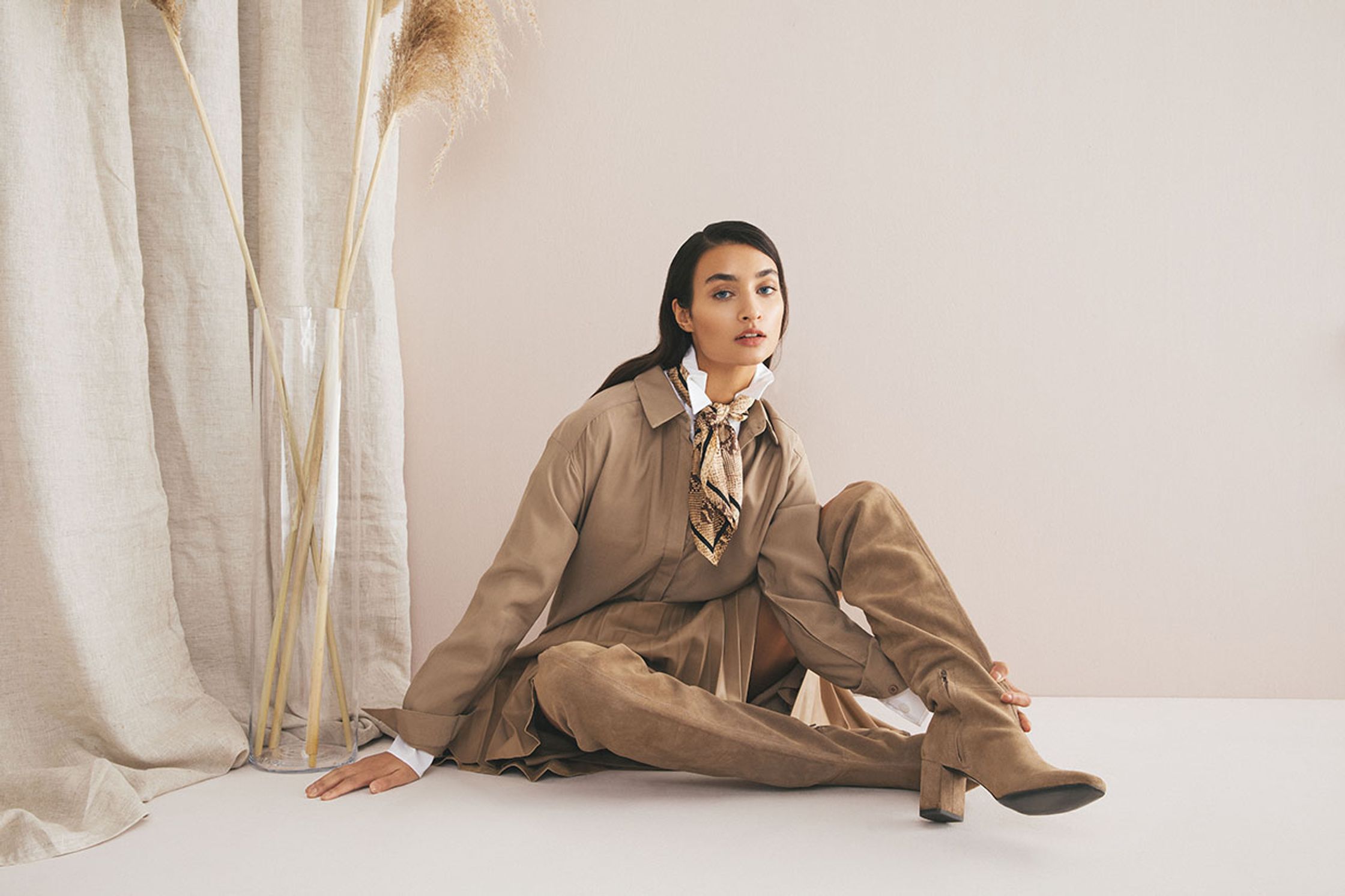 a woman sitting on the floor in a tan coat and thigh high boots