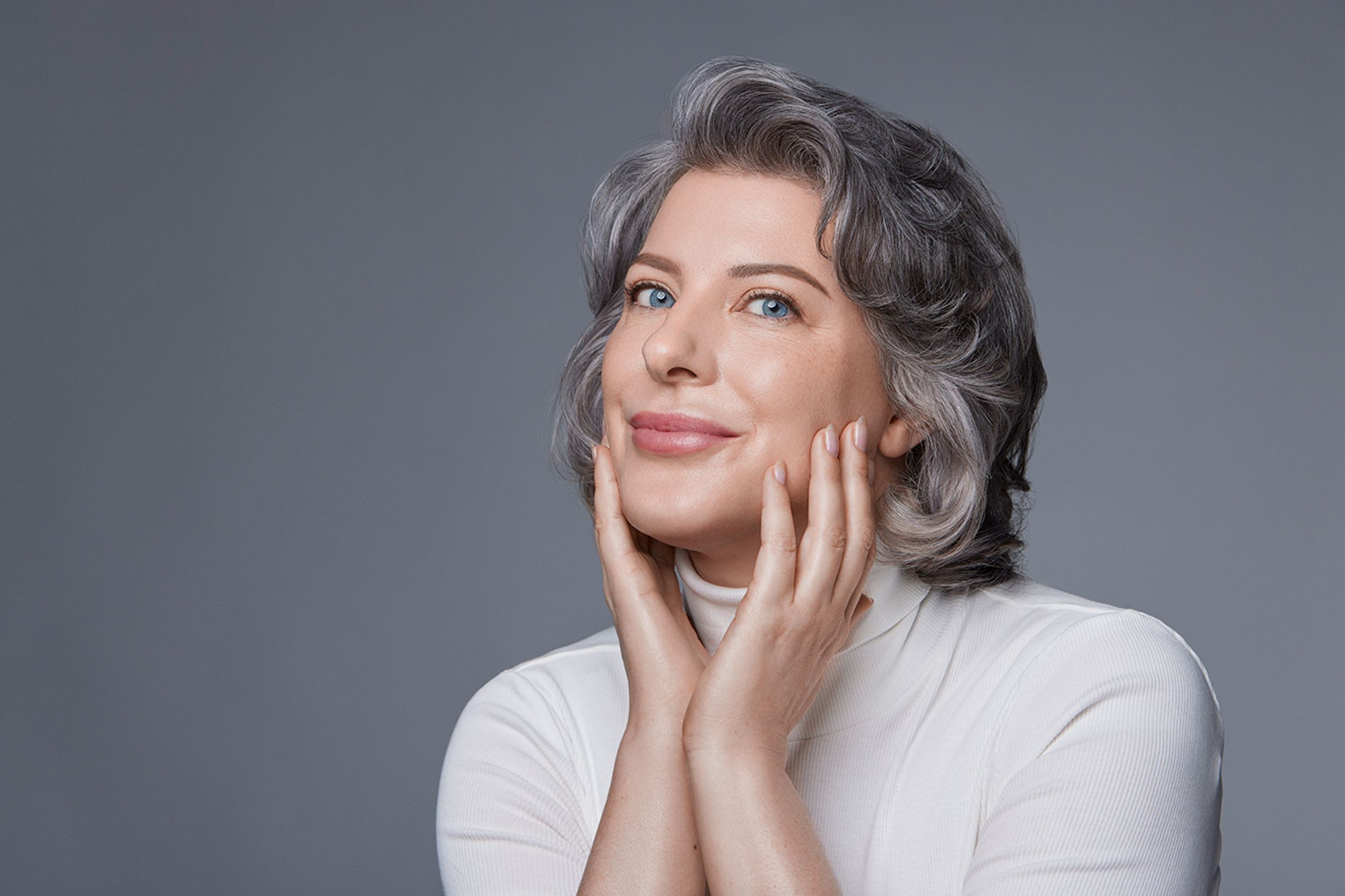 a woman with gray hair is posing with her hands on her face