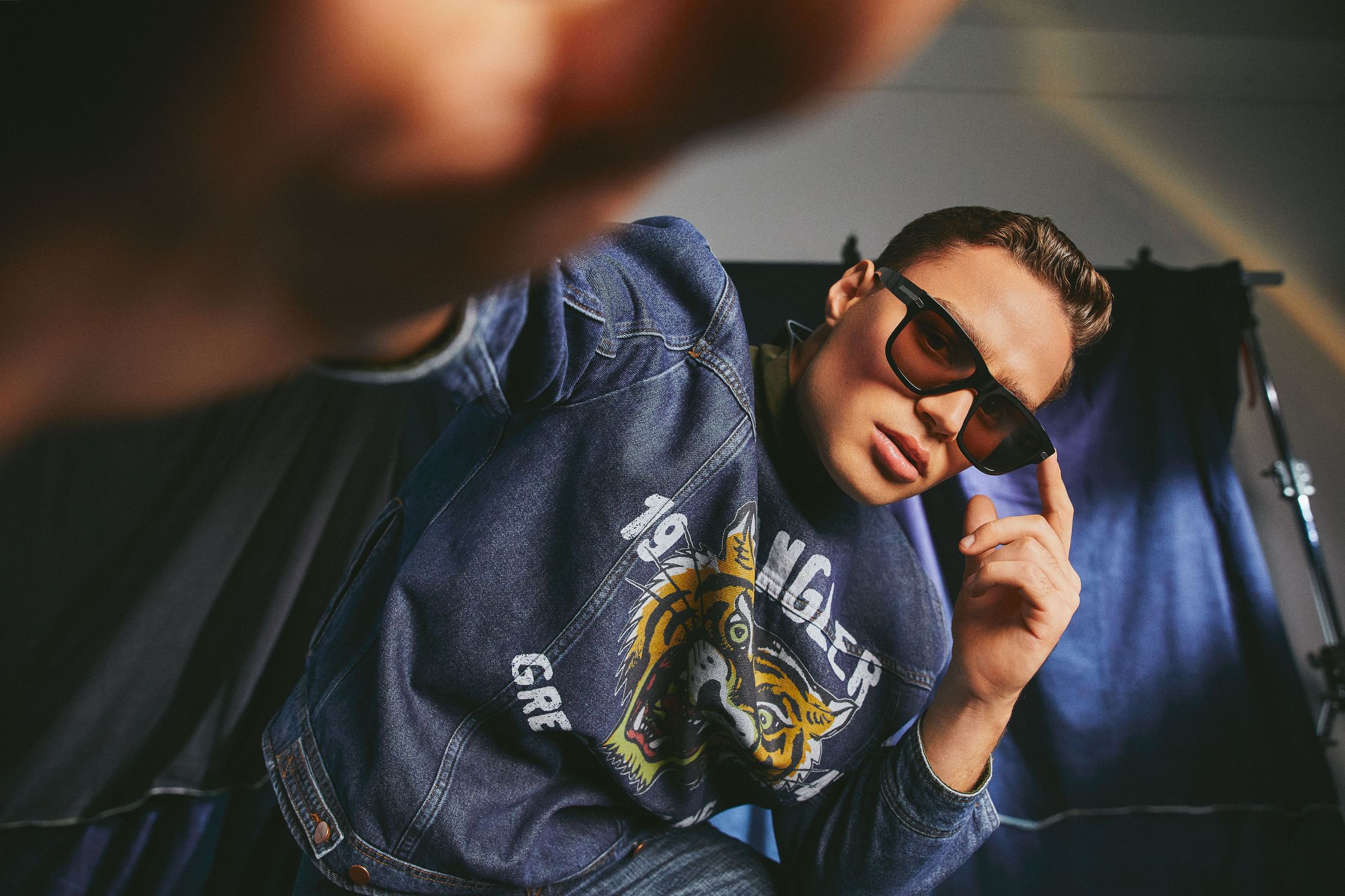 a man wearing sunglasses and a denim jacket posing for a photo