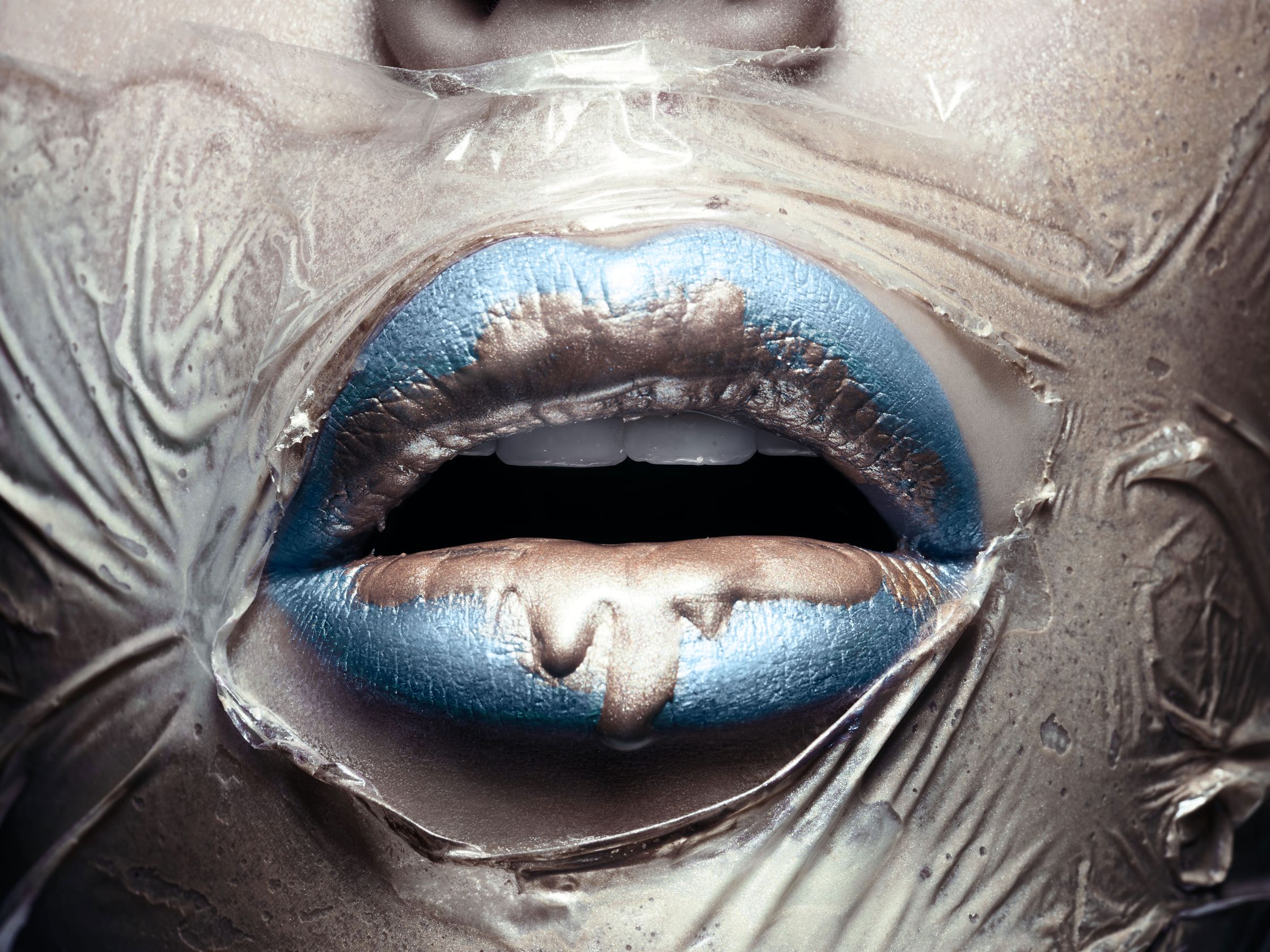 Close-up of lips painted in blue and silver, covered with plastic wrap, representing the restricted breath and struggle for survival amidst environmental degradation.