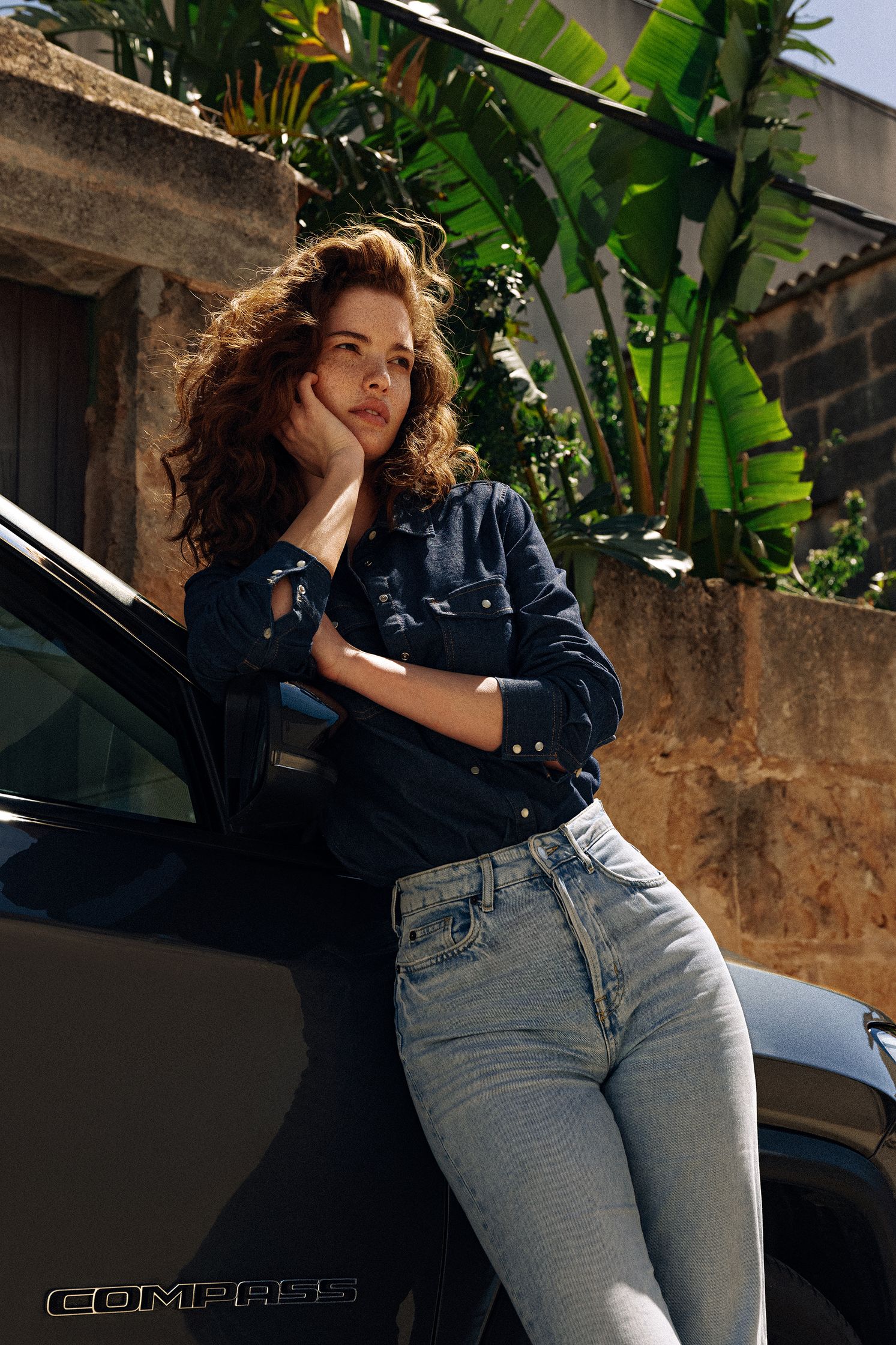 a woman in jeans leaning against a black suv