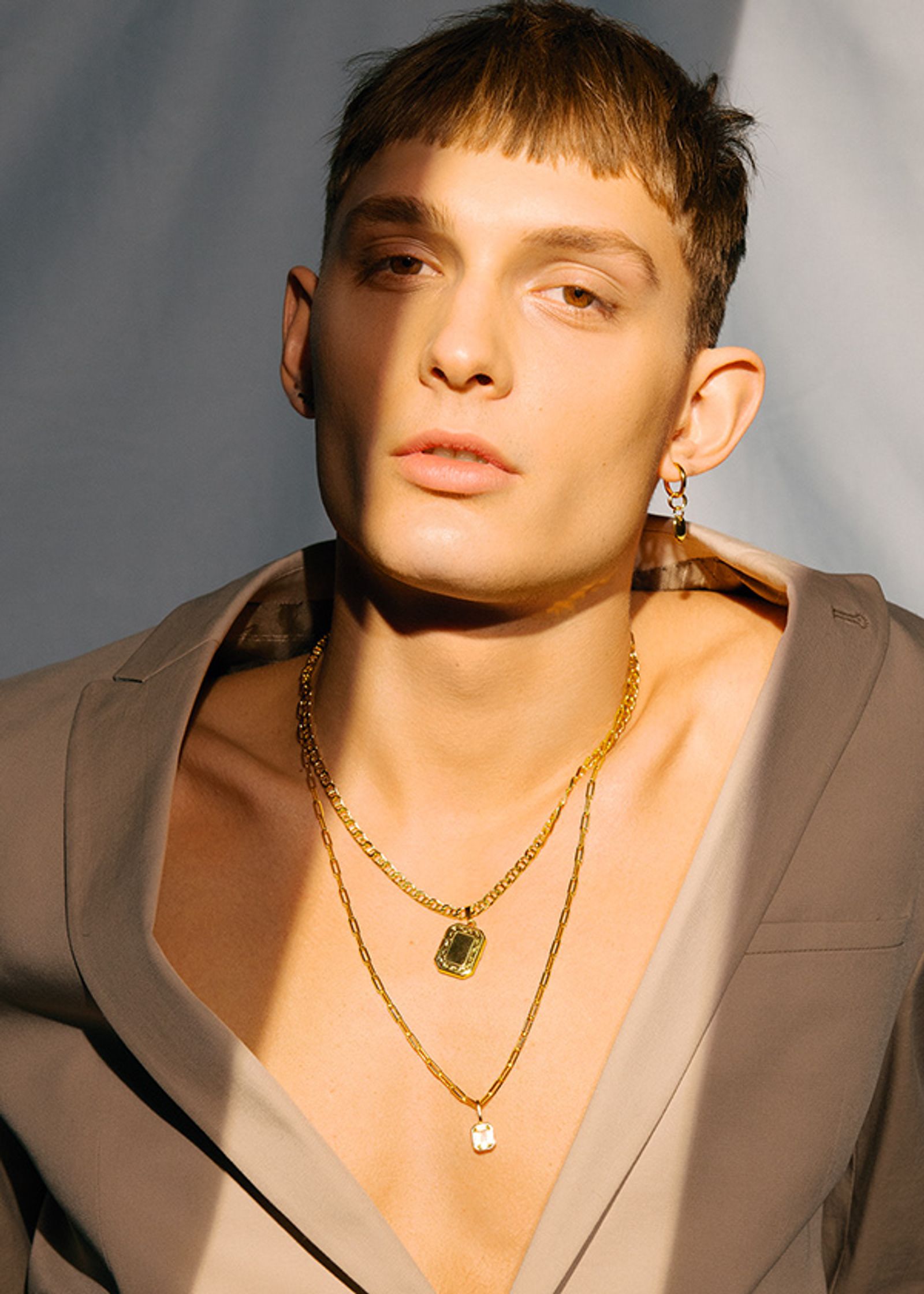 a man in a tan jacket with gold necklaces