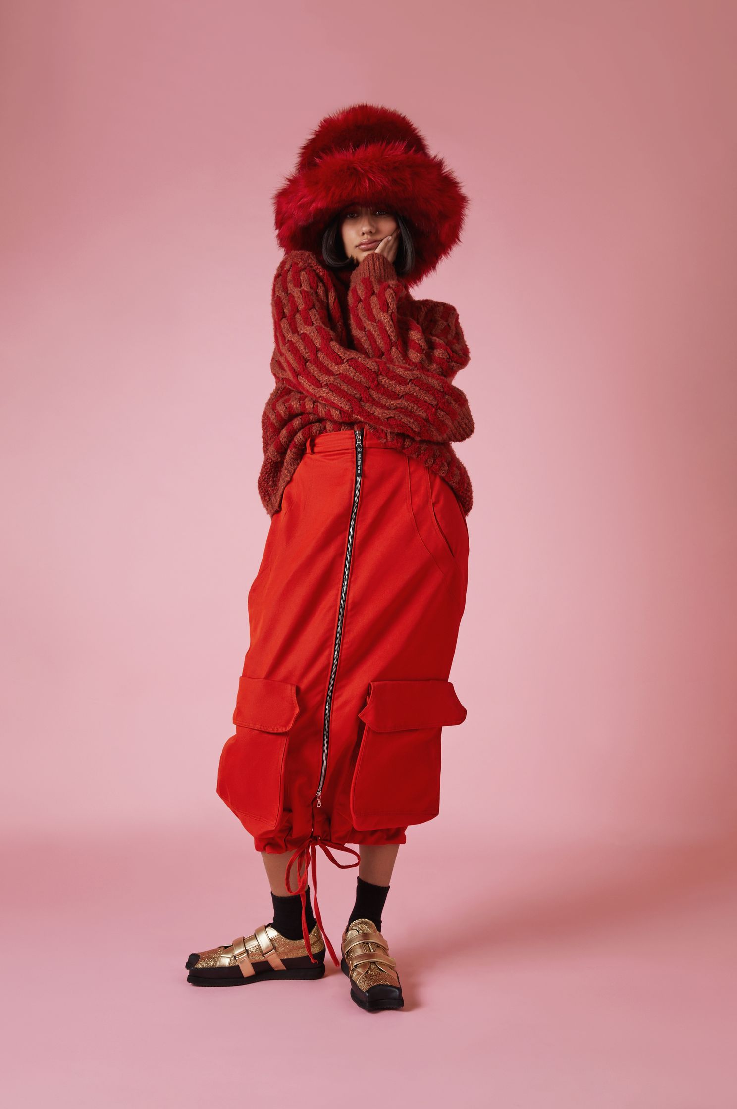 a woman in a red skirt and fur hat posing on a pink background