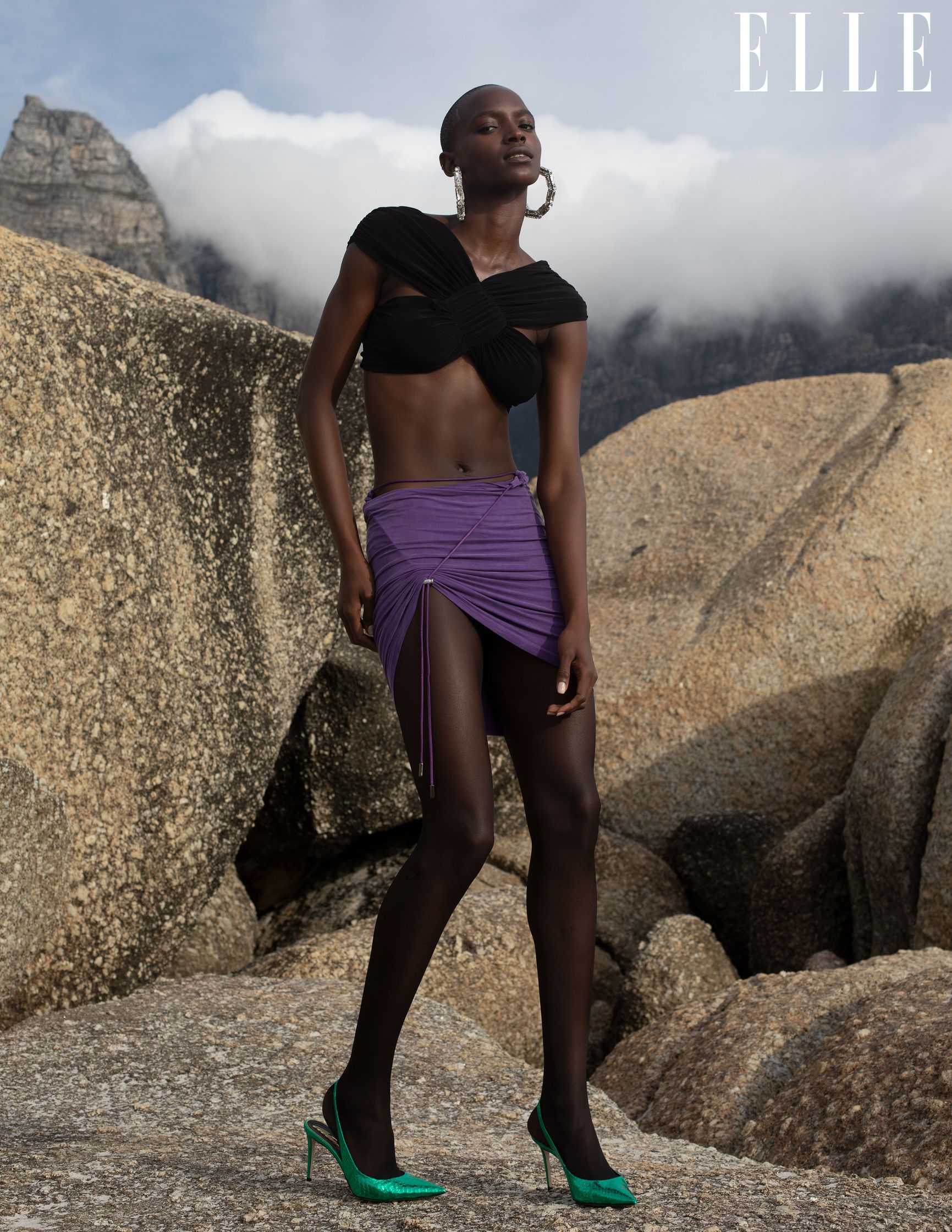 a woman in a black top and purple skirt posing on rocks