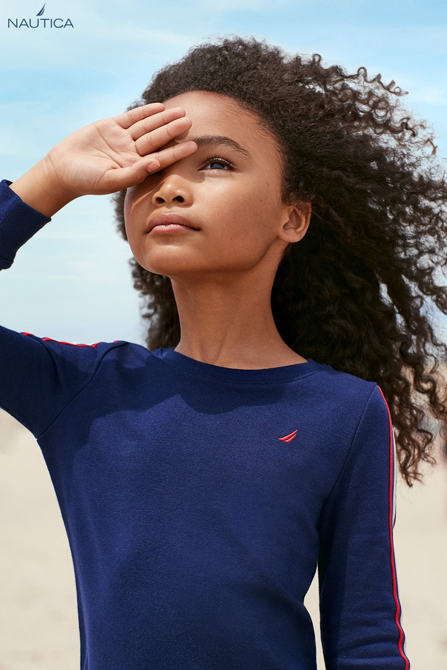 a young girl is standing on the beach in a blue shirt
