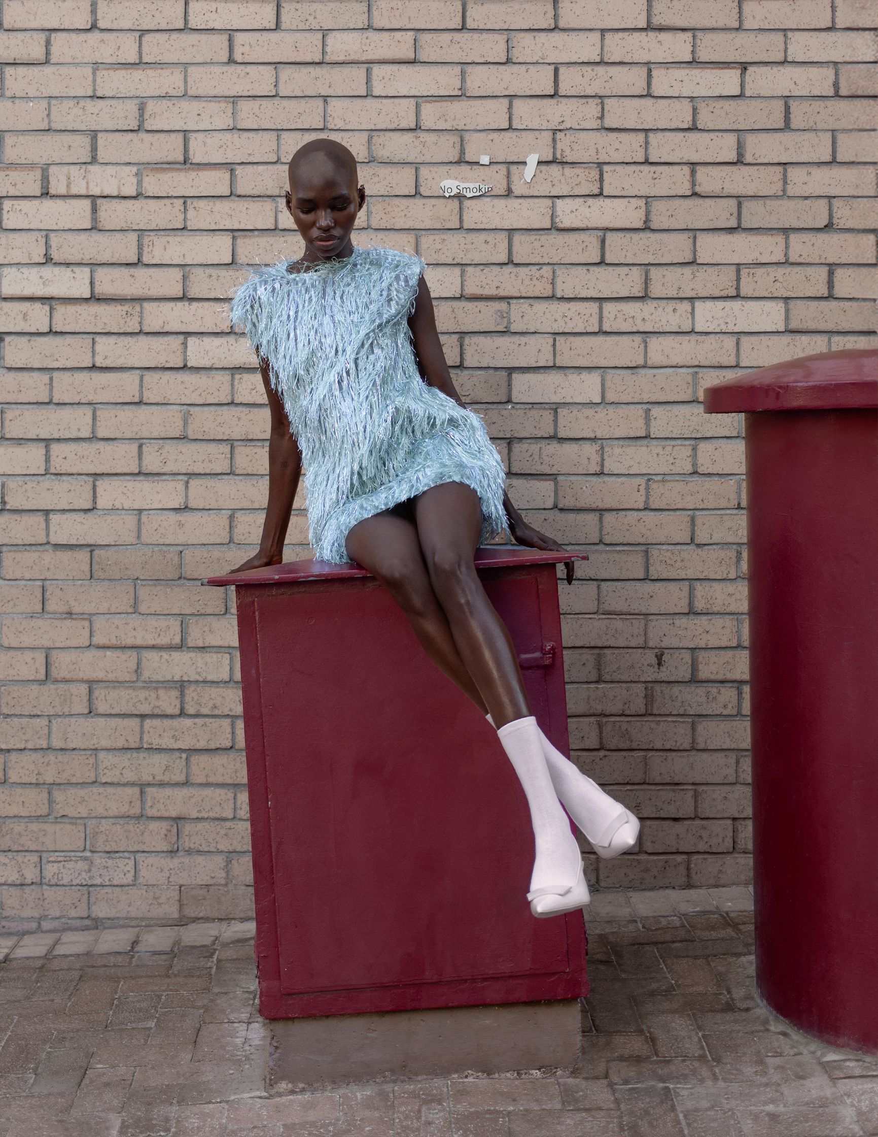 a woman in a blue dress sitting on top of a red trash can