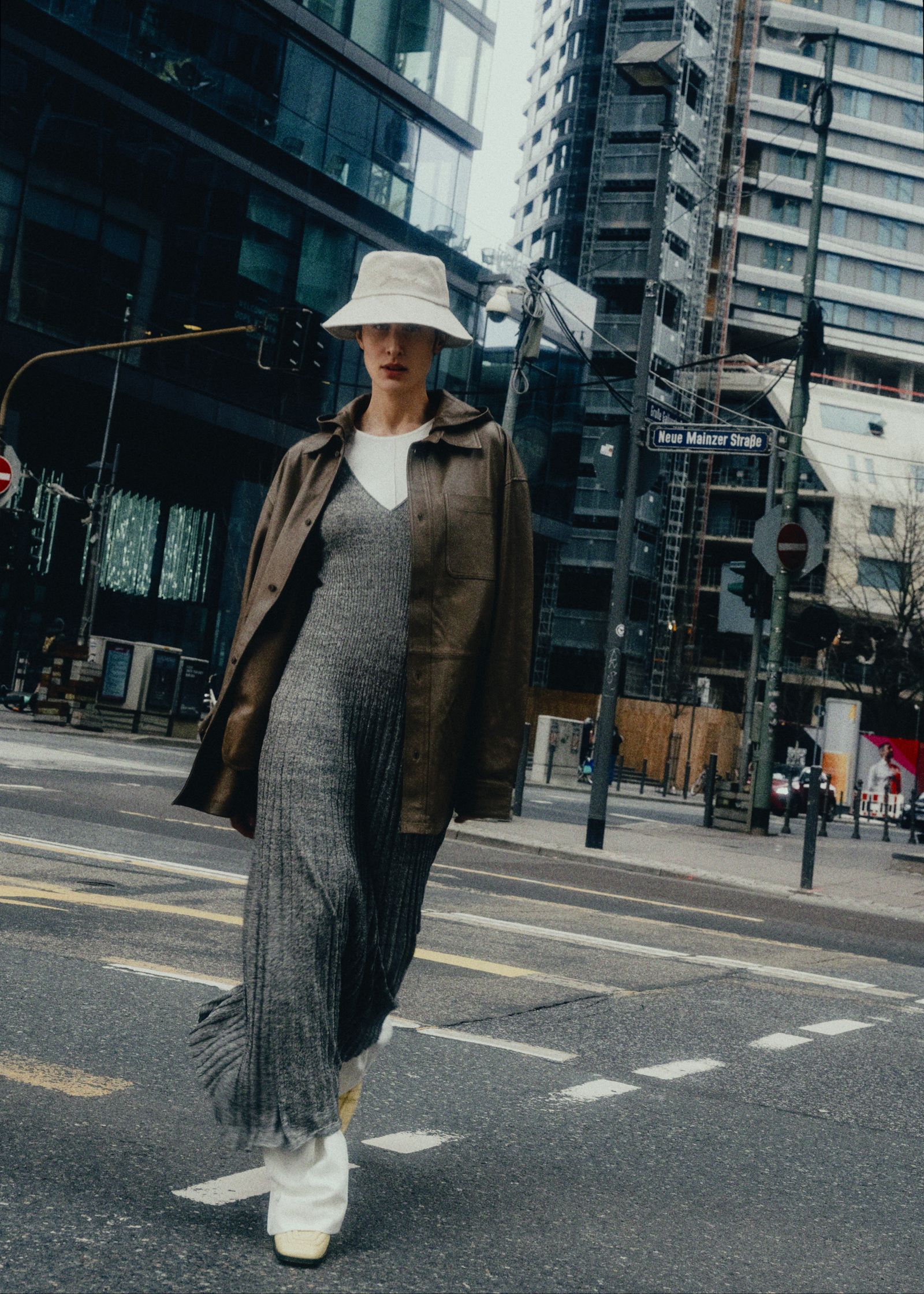 a woman in a grey dress and hat crossing the street