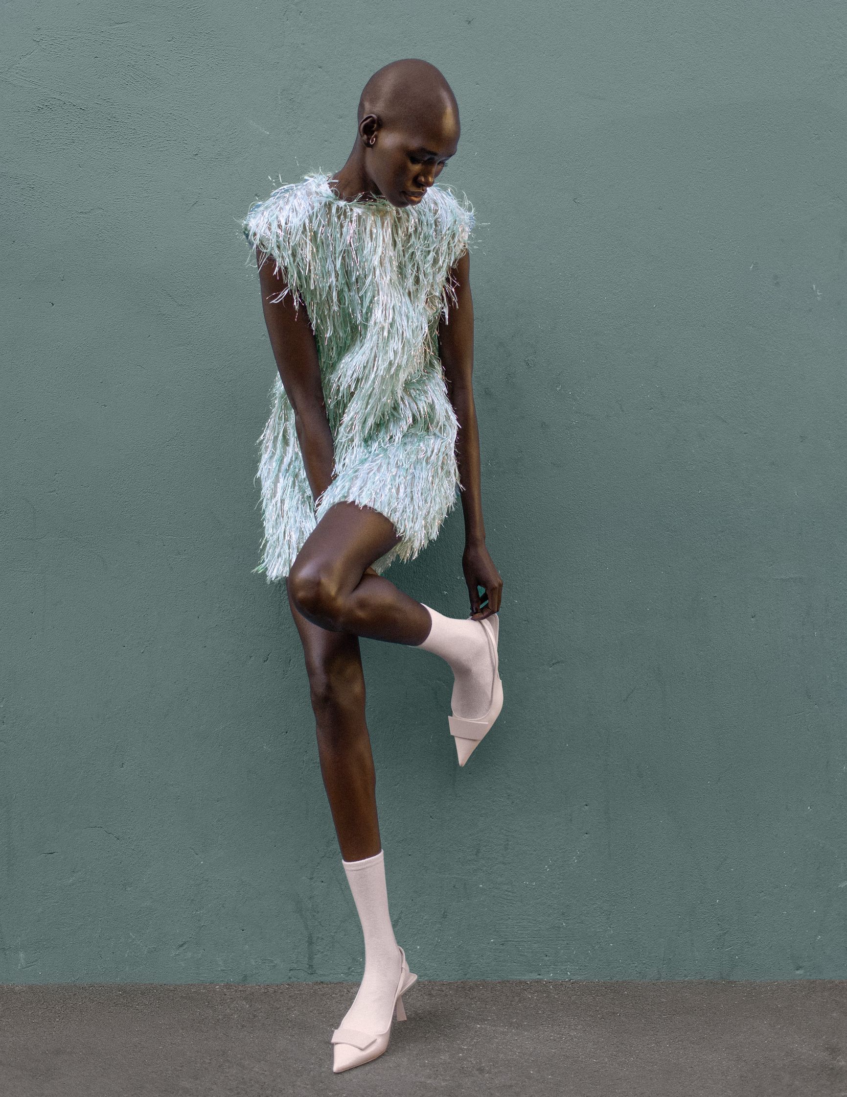 a woman in a feathered dress posing on a green wall