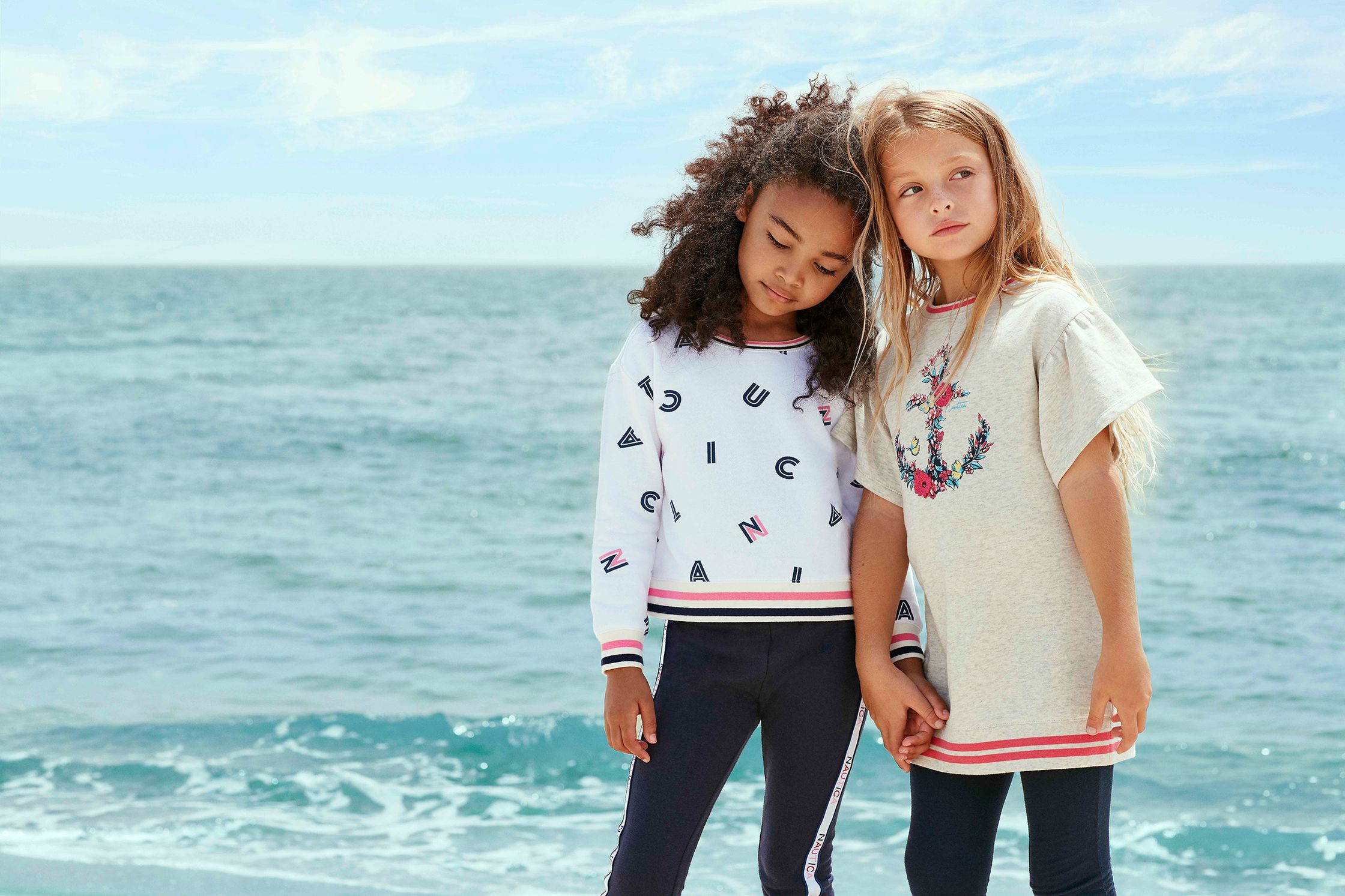 two young girls standing on the beach next to the ocean