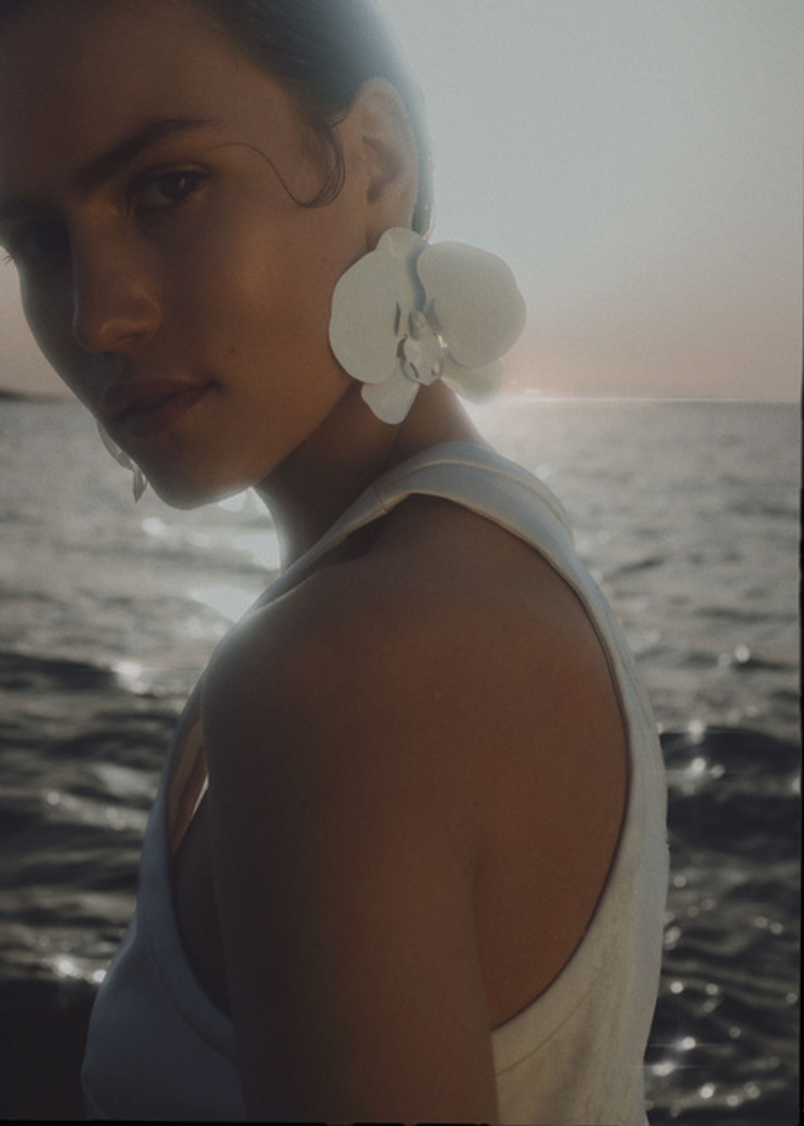a woman wearing a white top and a pair of white earrings