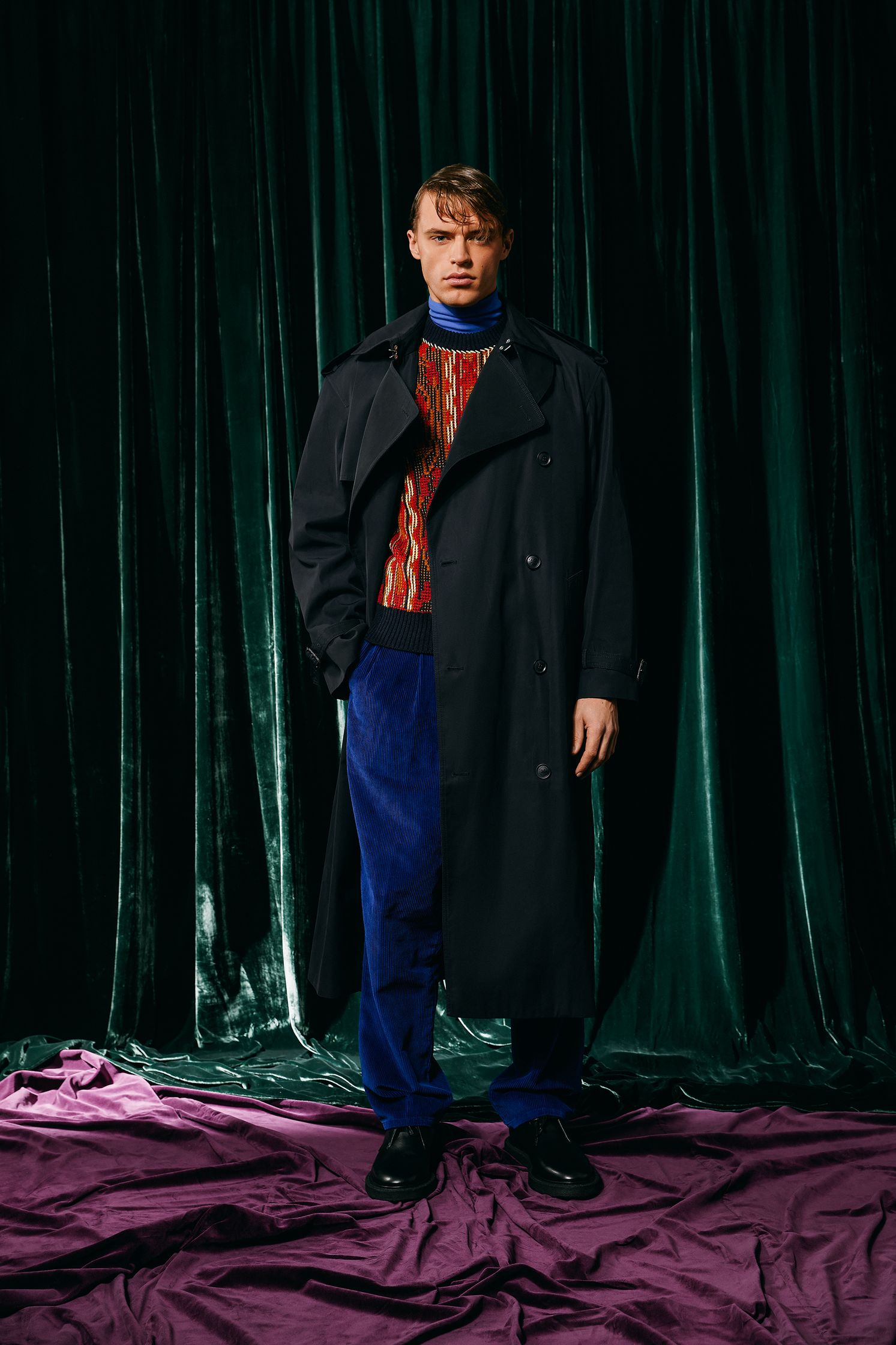 a man in a trench coat standing in front of a purple curtain