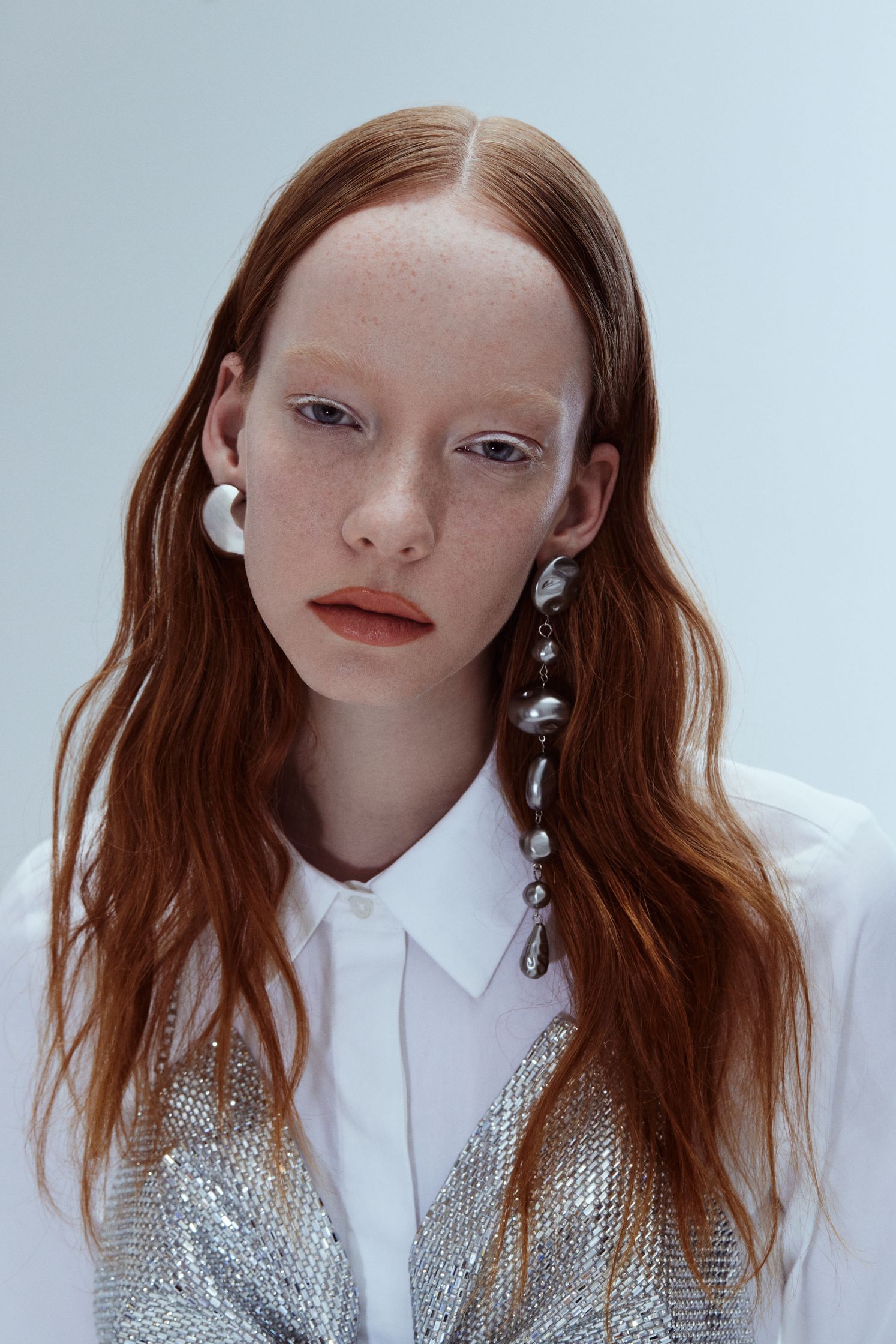 a woman with red hair wearing a white shirt and silver earrings