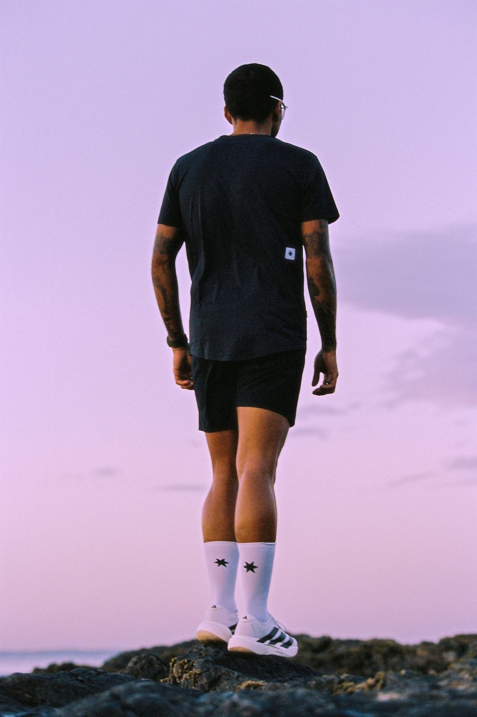 a man standing on rocks at sunset wearing black shorts and a black t - shirt by advertising photographer Martin Kula