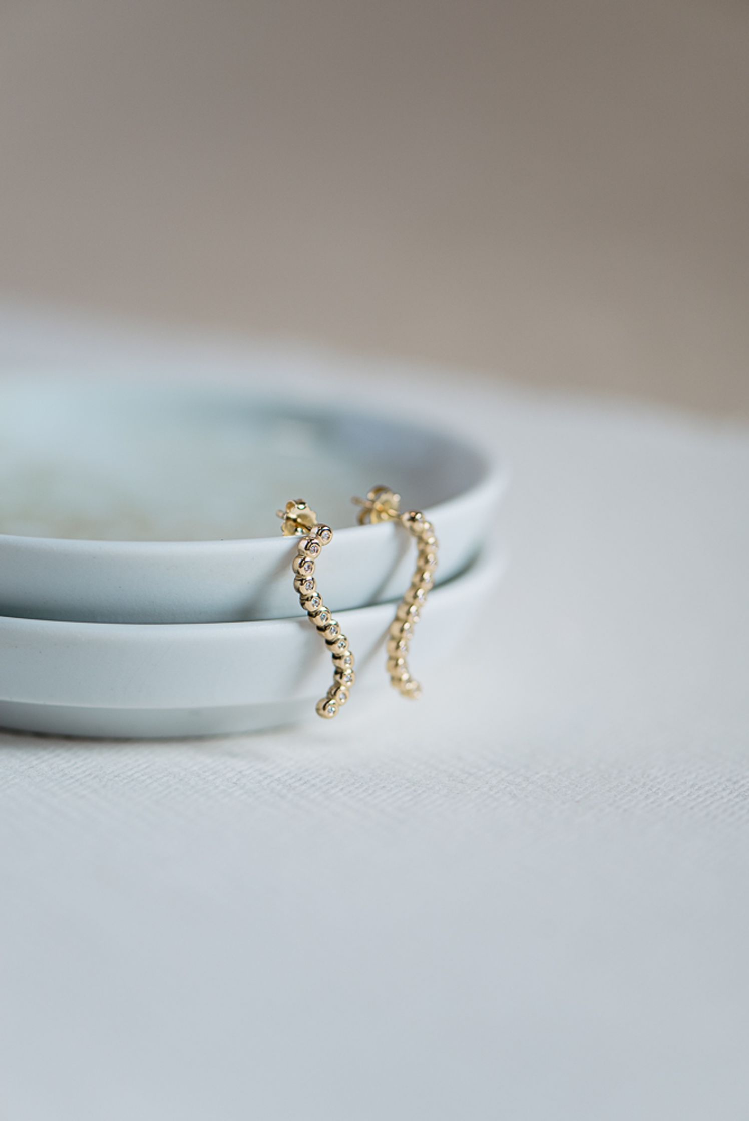 a pair of gold plated earrings sitting on a plate by maren jewellery