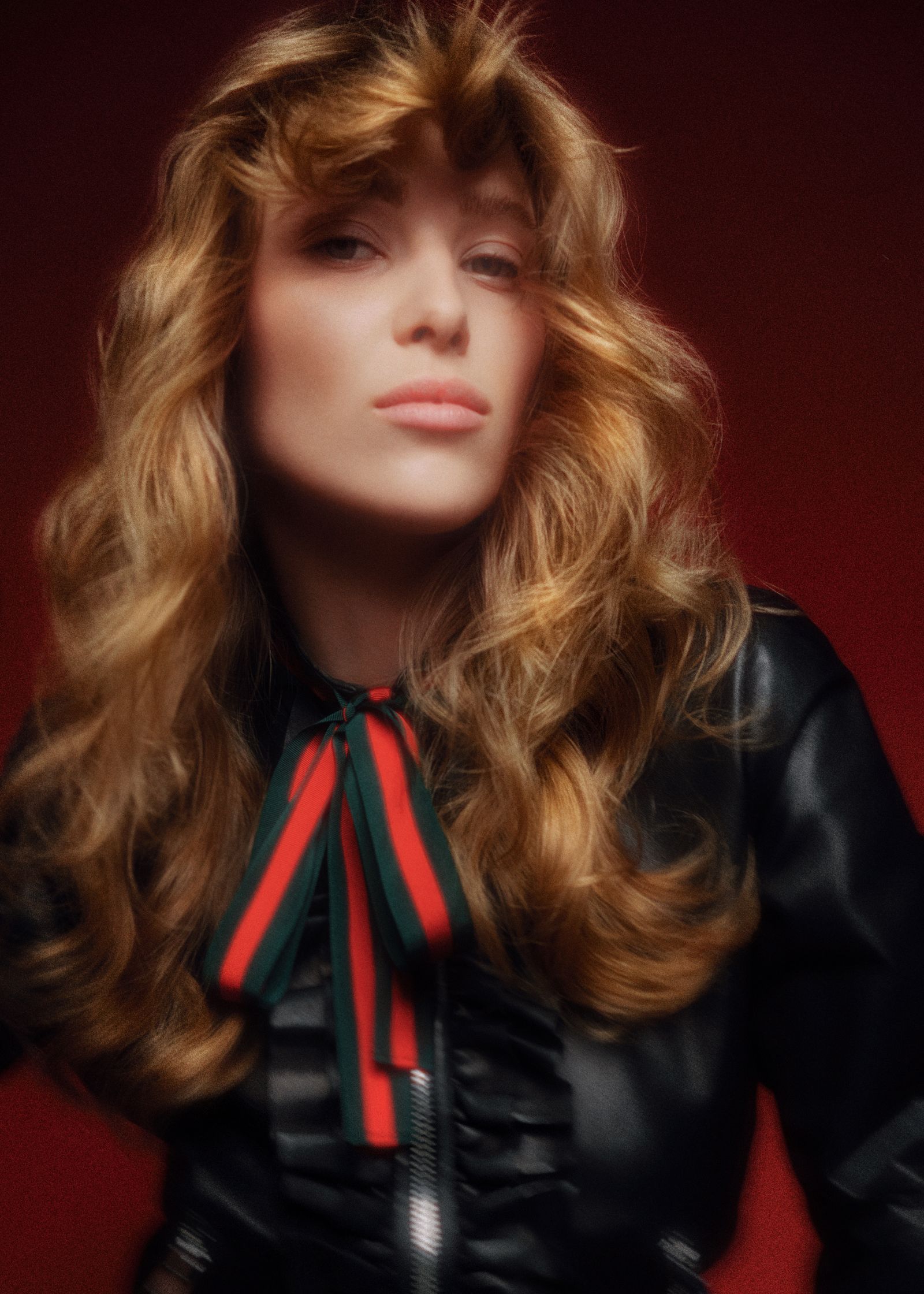 a woman in a leather jacket posing with a red background