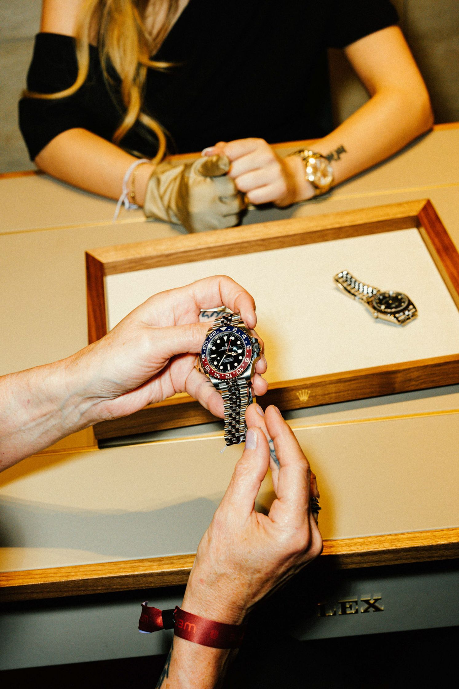 Hände-Detail beim Übergeben einer schwarzen Rolex-Uhr über dem Verkäufer-Tablett, Rolex-Logo auf dem Tray sichtbar, Beratungsmoment Rolex Boutique Berlin
